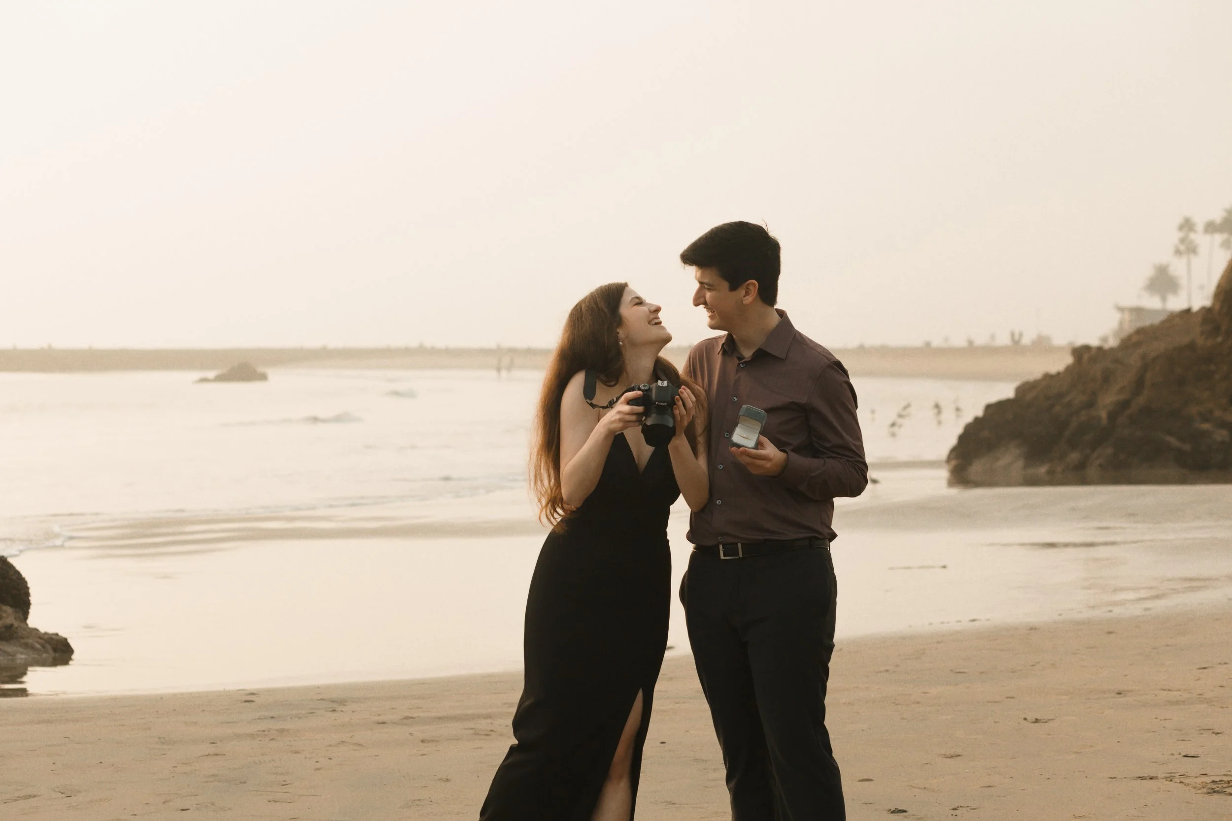 candid photo of couple laughing while looking at camera on the beach in newport for their proposal