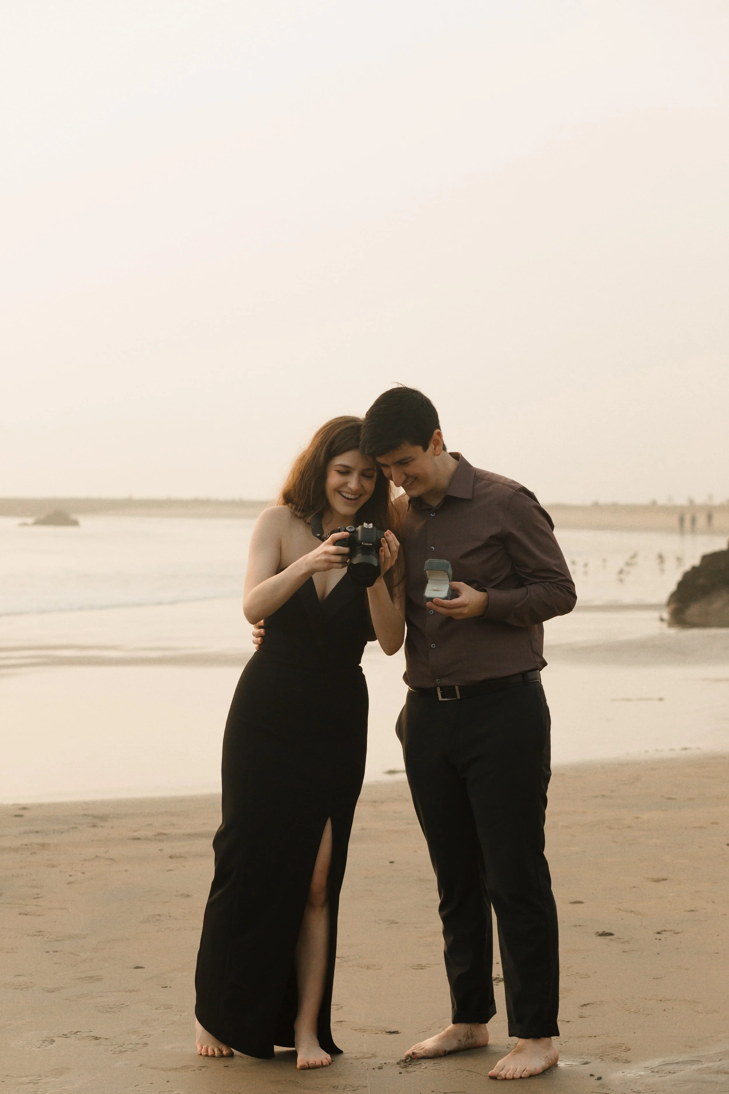 couple looking at their camera candid while guy is holding ring box from their proposal in newport beach