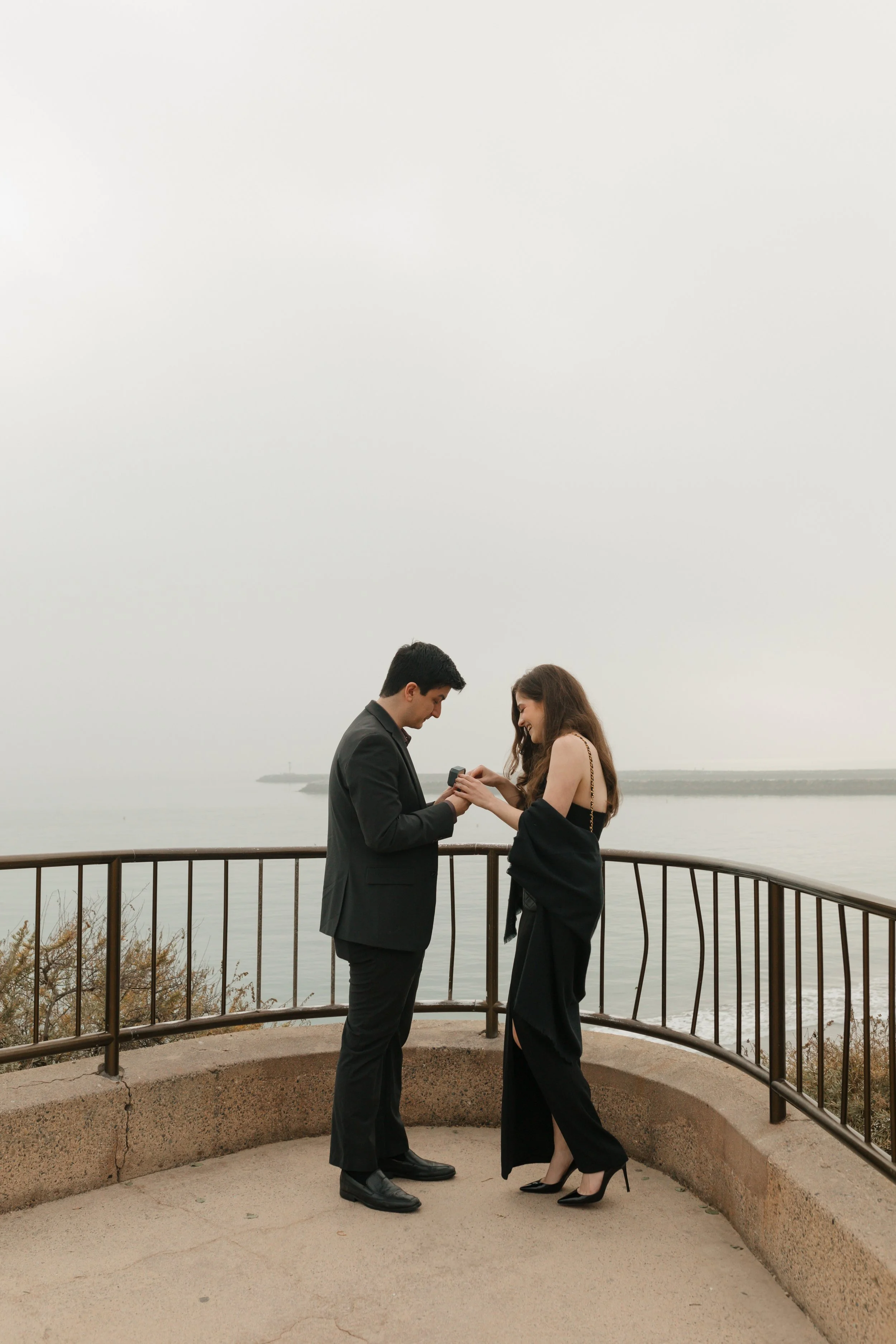 couple looking at ring from proposal at lookout in newport beach with the ocean in background