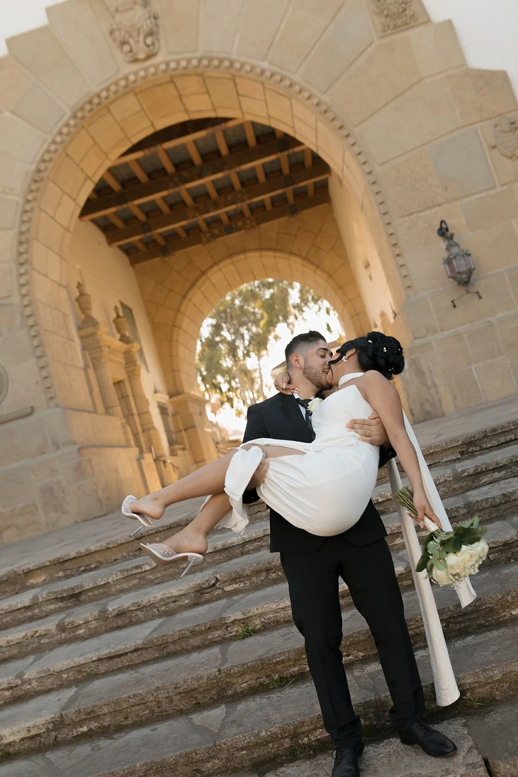 Candid romantic moment at the Santa Barbara Courthouse stone stairs, groom carrying the bride in his arms as he walks away, capturing an intimate, joyful elopement scene with natural movement and connection.