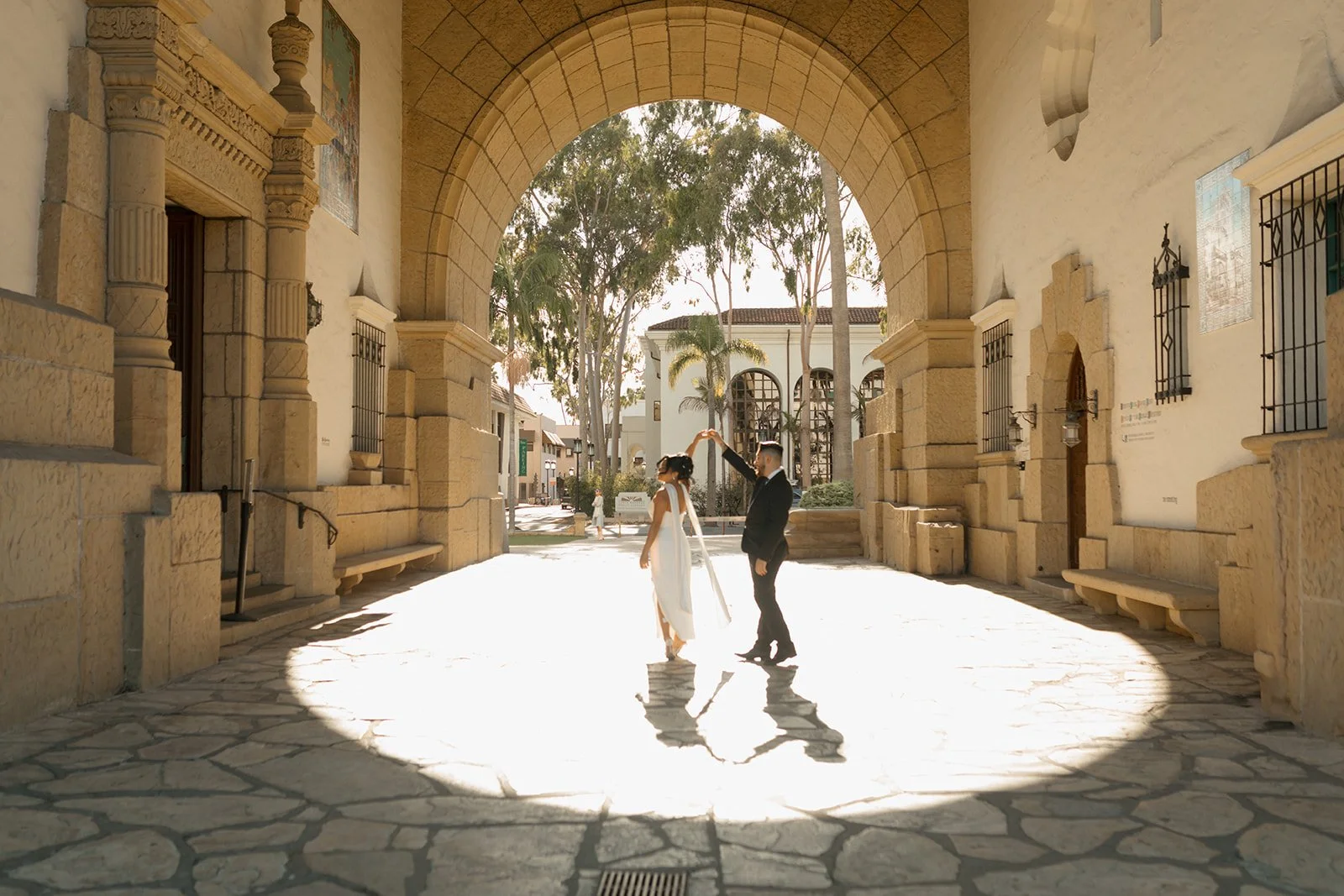 Couple dancing beneath the iconic archway at the Santa Barbara Courthouse, the groom spinning the bride in a playful, intimate moment during their private celebration