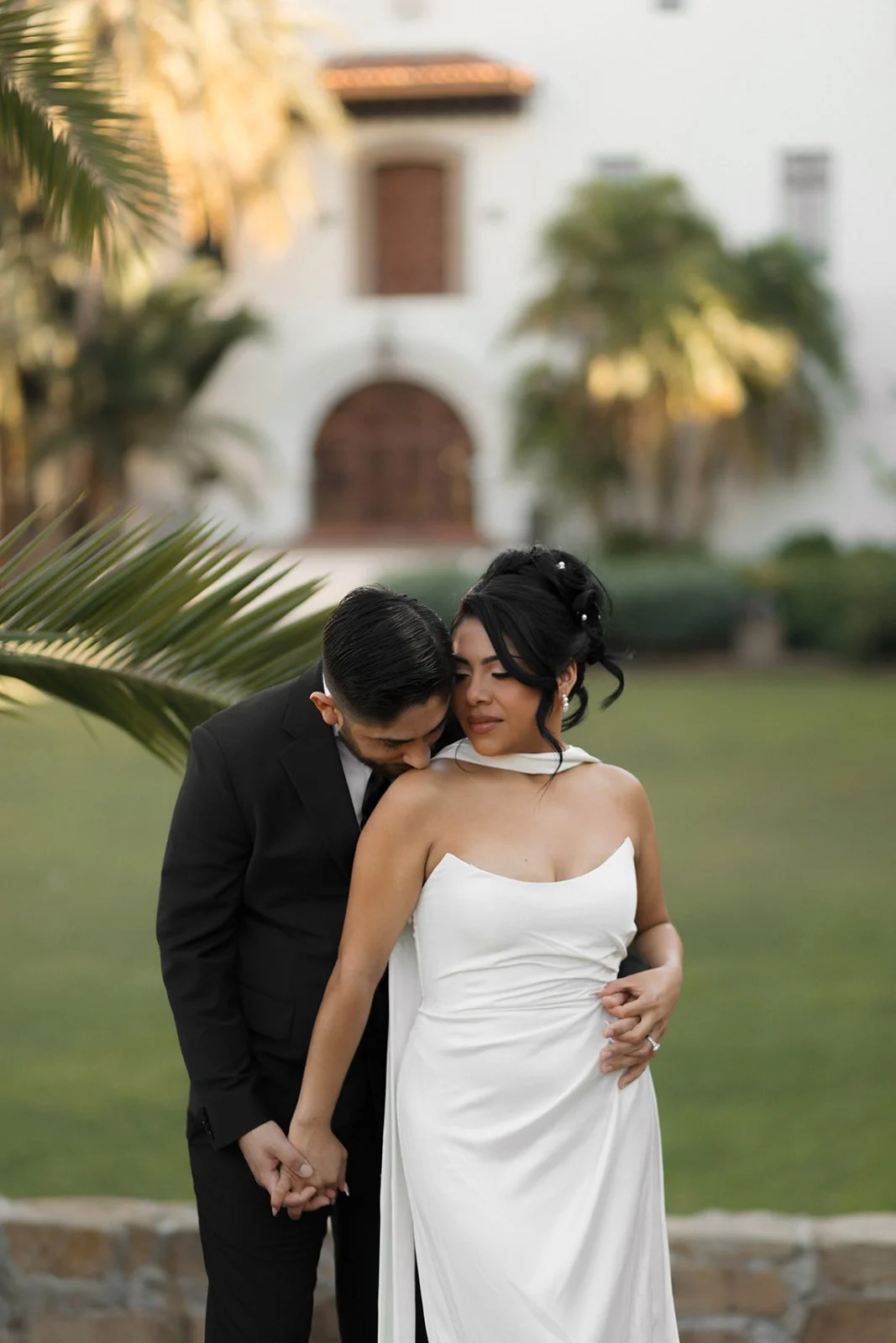 Groom hugging bride from behind in the Santa Barbara Courthouse gardens, kissing her shoulder in an intimate romantic elopement moment