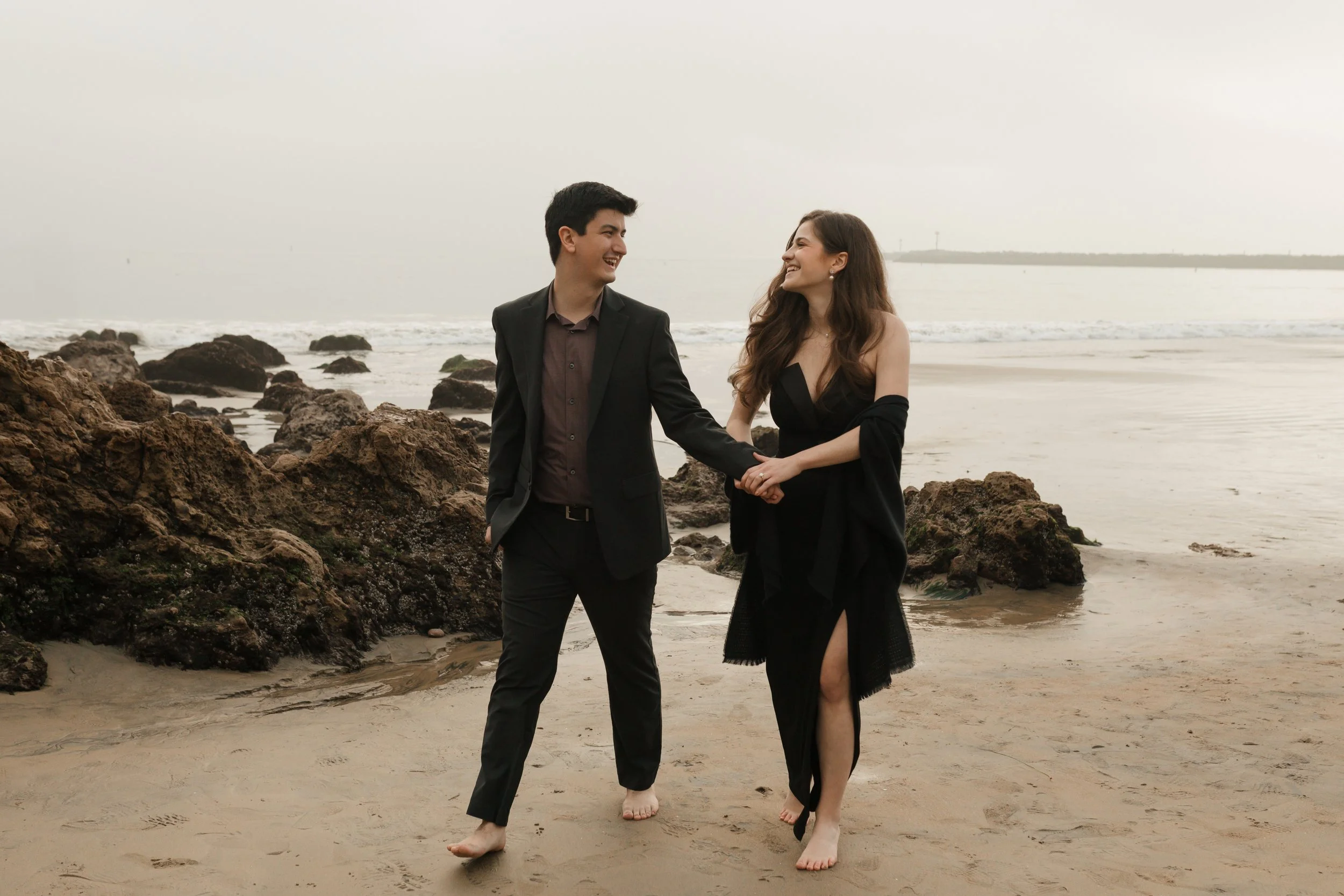 couple holding hands walking away  in newport beach from proposal