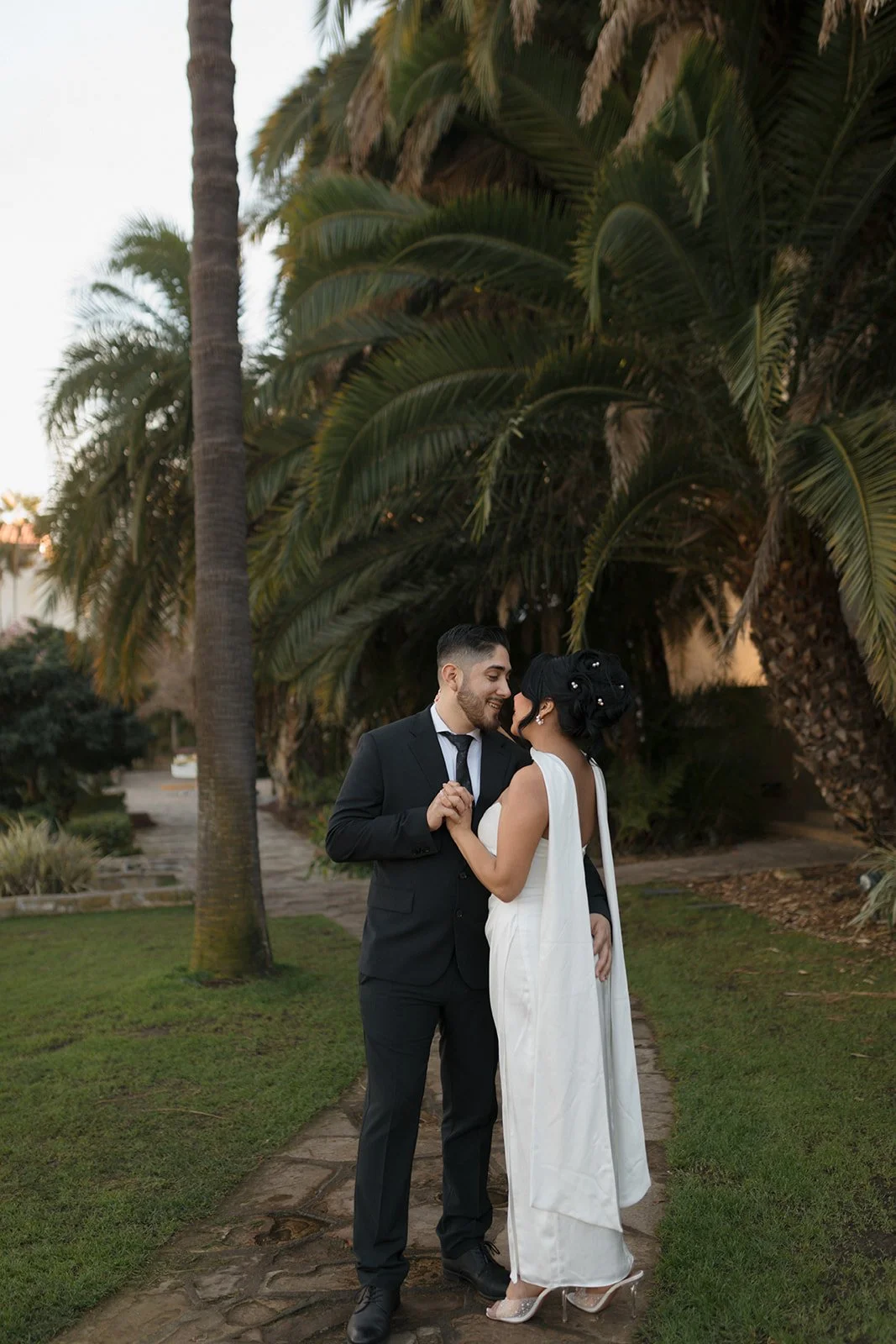 Couple holding hands facing each other from a distance during elopement at the Santa Barbara Courthouse Sunken Gardens, bride with her back to the camera while groom holds her at the waist and looks at her