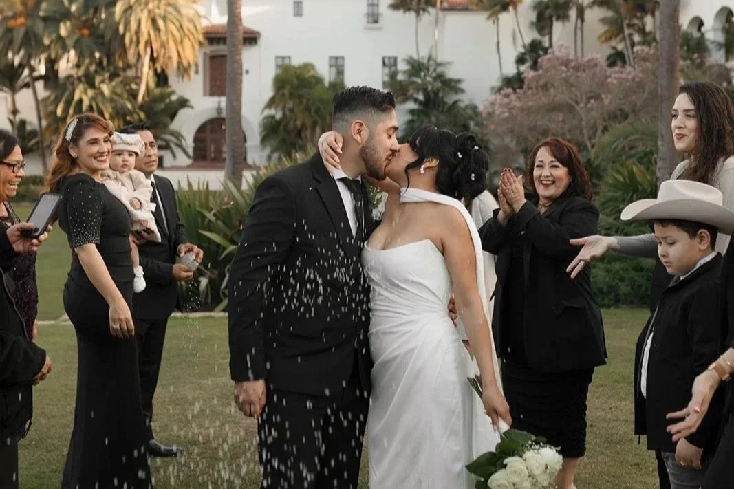 Couple sharing a kiss as they exit ceremony at the Santa Barbara Courthouse Sunken Gardens, with family throwing rice in celebration behind them