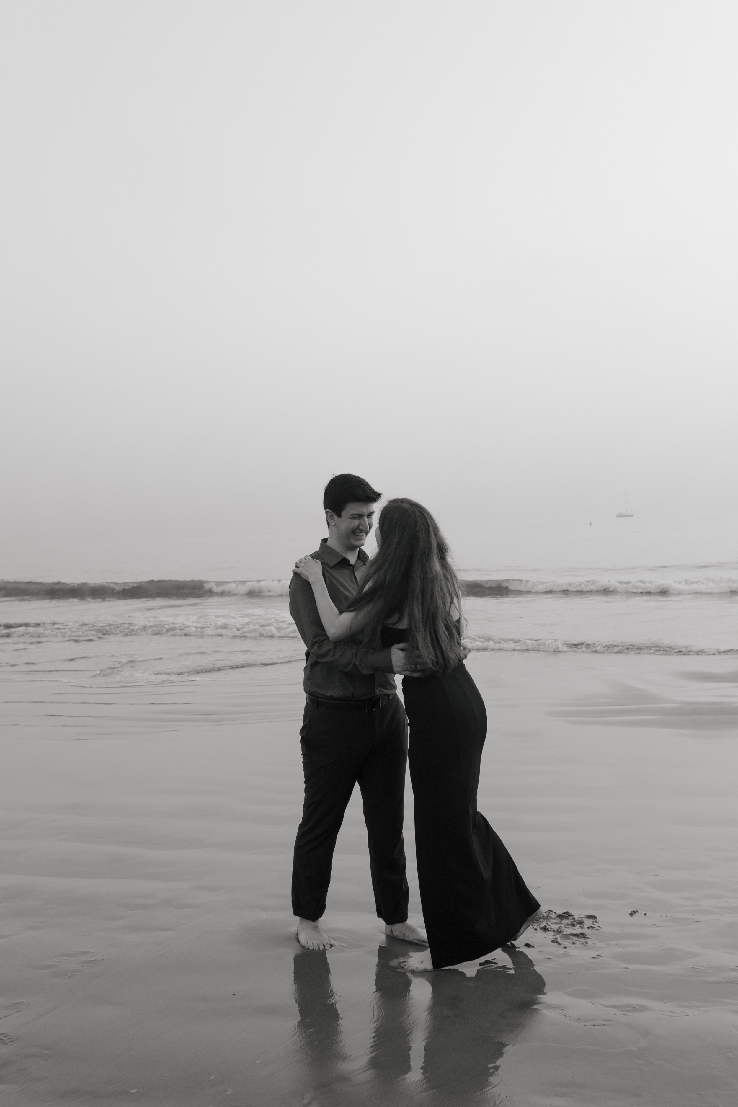 black and white photo of couple candd falling into eachothers arms at newport beach from their proposal