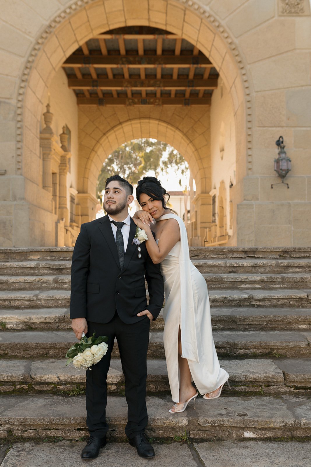 ditorial elopement photo at the Santa Barbara Courthouse steps and arch, groom holding bouquet as bride leans into him in a romantic, posed moment.