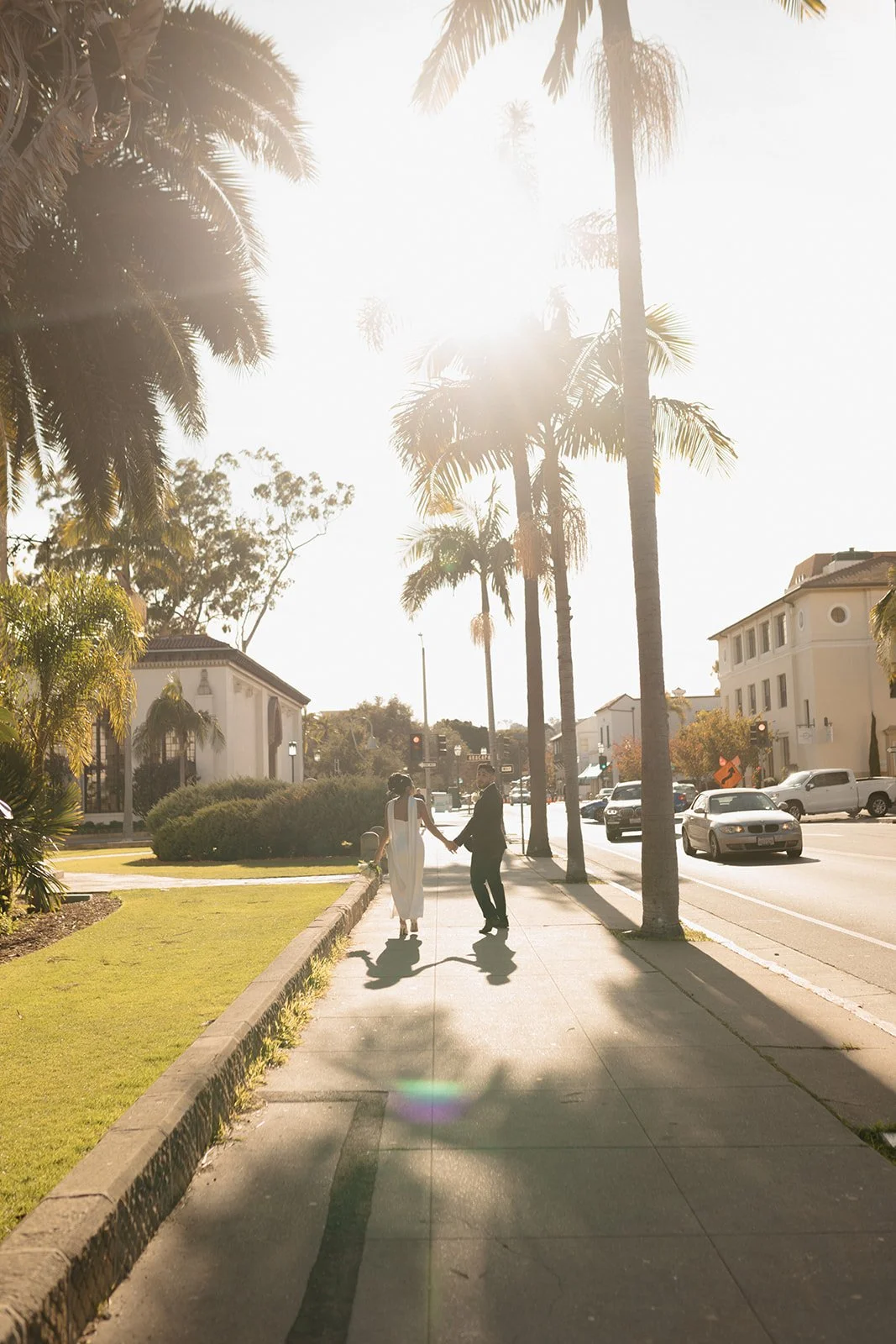 couple walking next to the santa barbrara courthosue, golden hour as groom likes back to camera and bride looking at him.