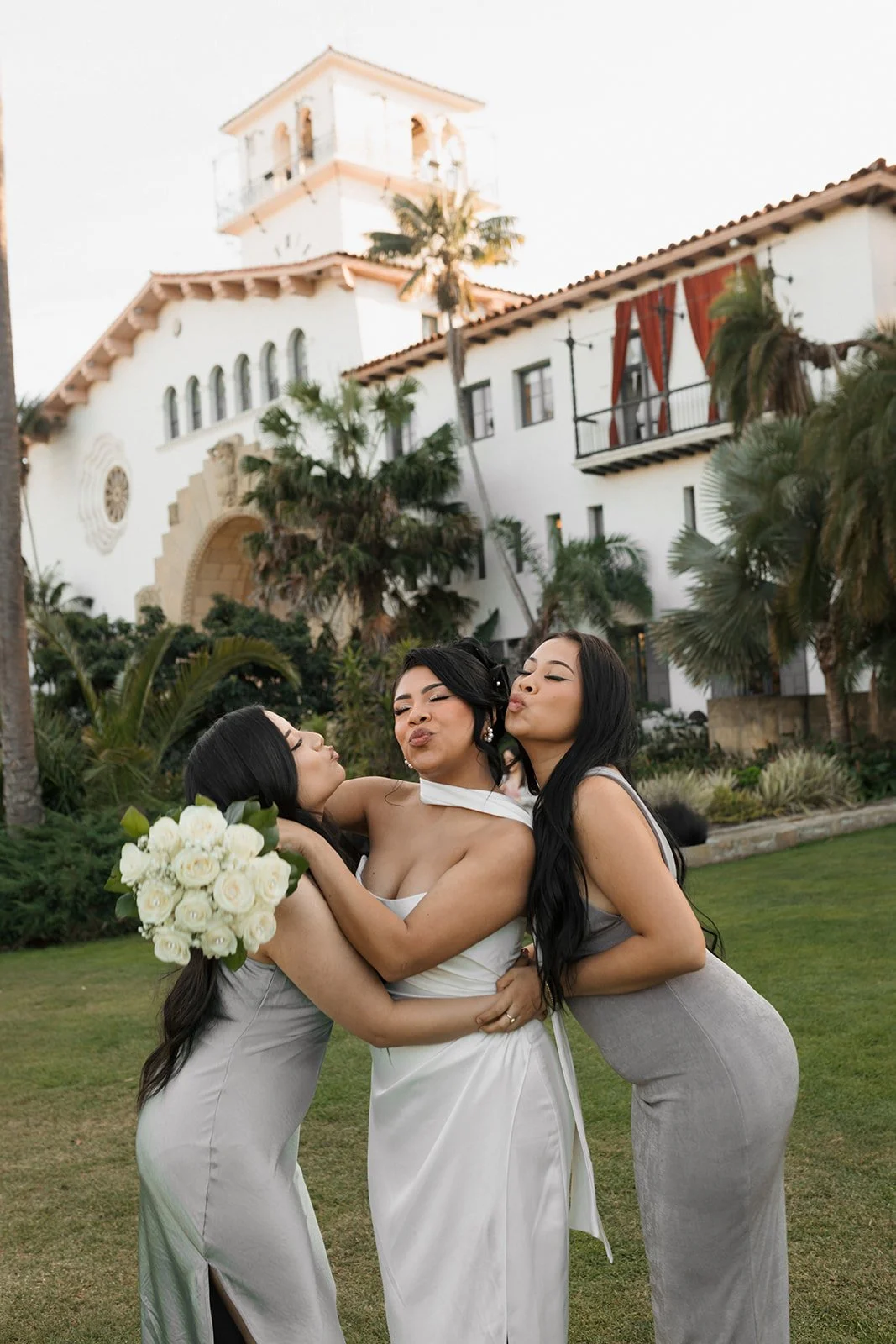 Bride and her two best friends hugging and making kissy faces in a candid celebratory moment at the Santa Barbara Courthouse Sunken Gardens after the ceremony
