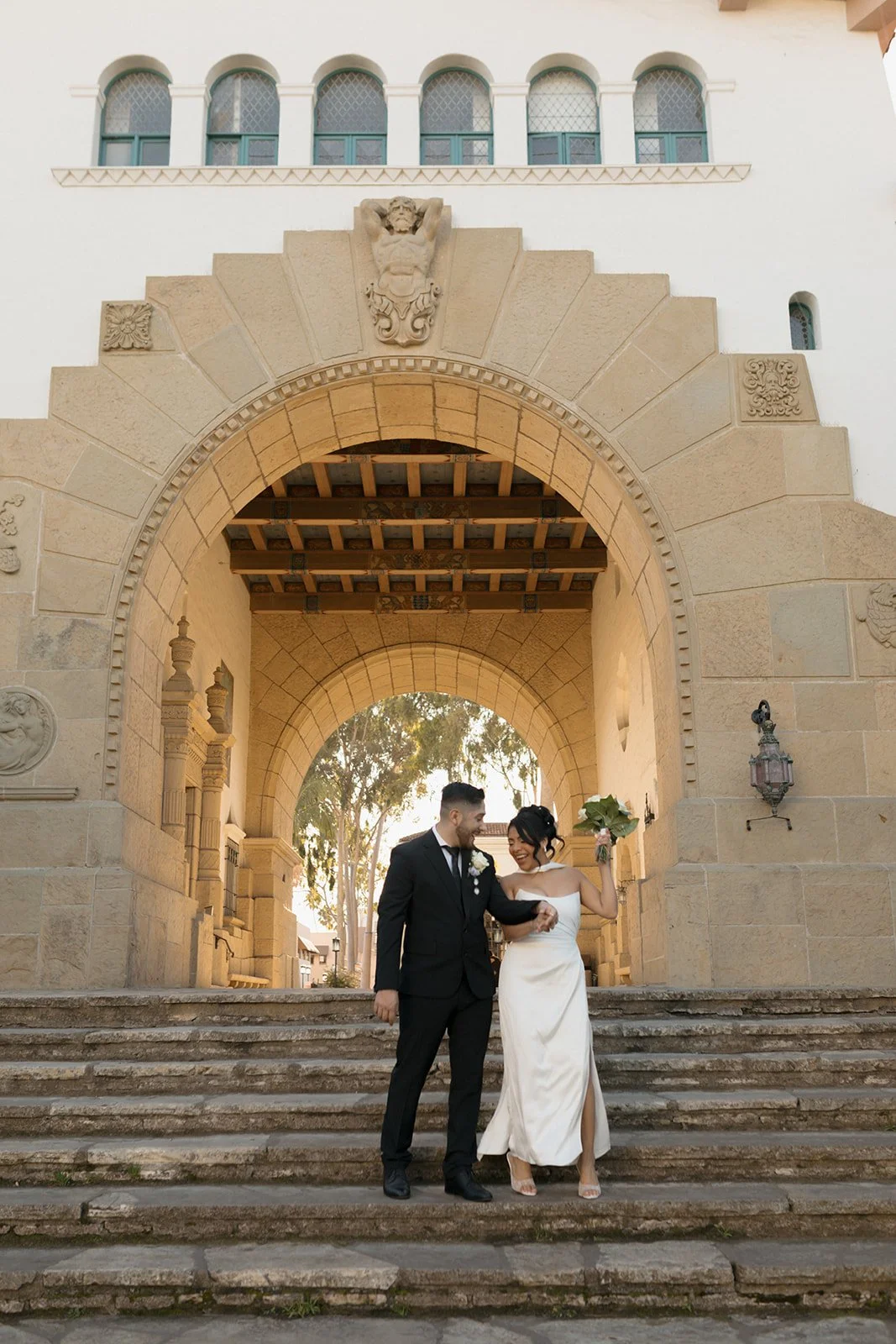 Candid elopement moment of a couple walking down stone steps, holding hands as their hips gently bump in a playful, natural rhythm, capturing movement, laughter, and an effortless romantic connection.