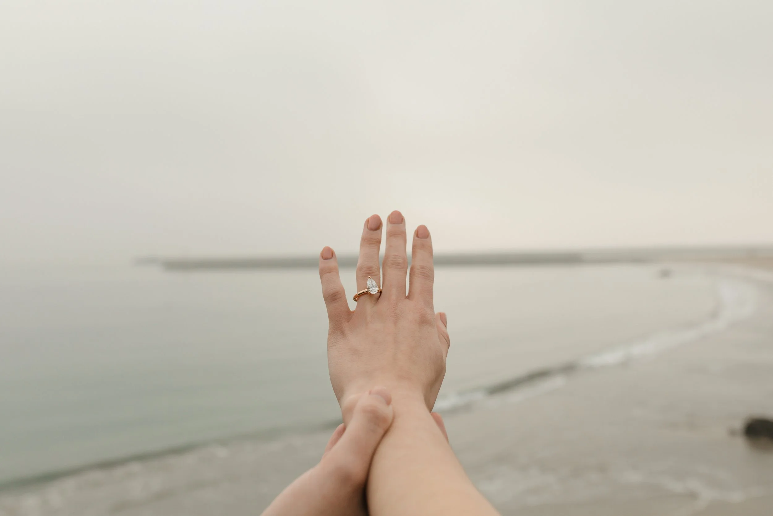 close up detail photo of the girls hand showing off the ring from the proposal at lookout in newport beach with the ocean in background