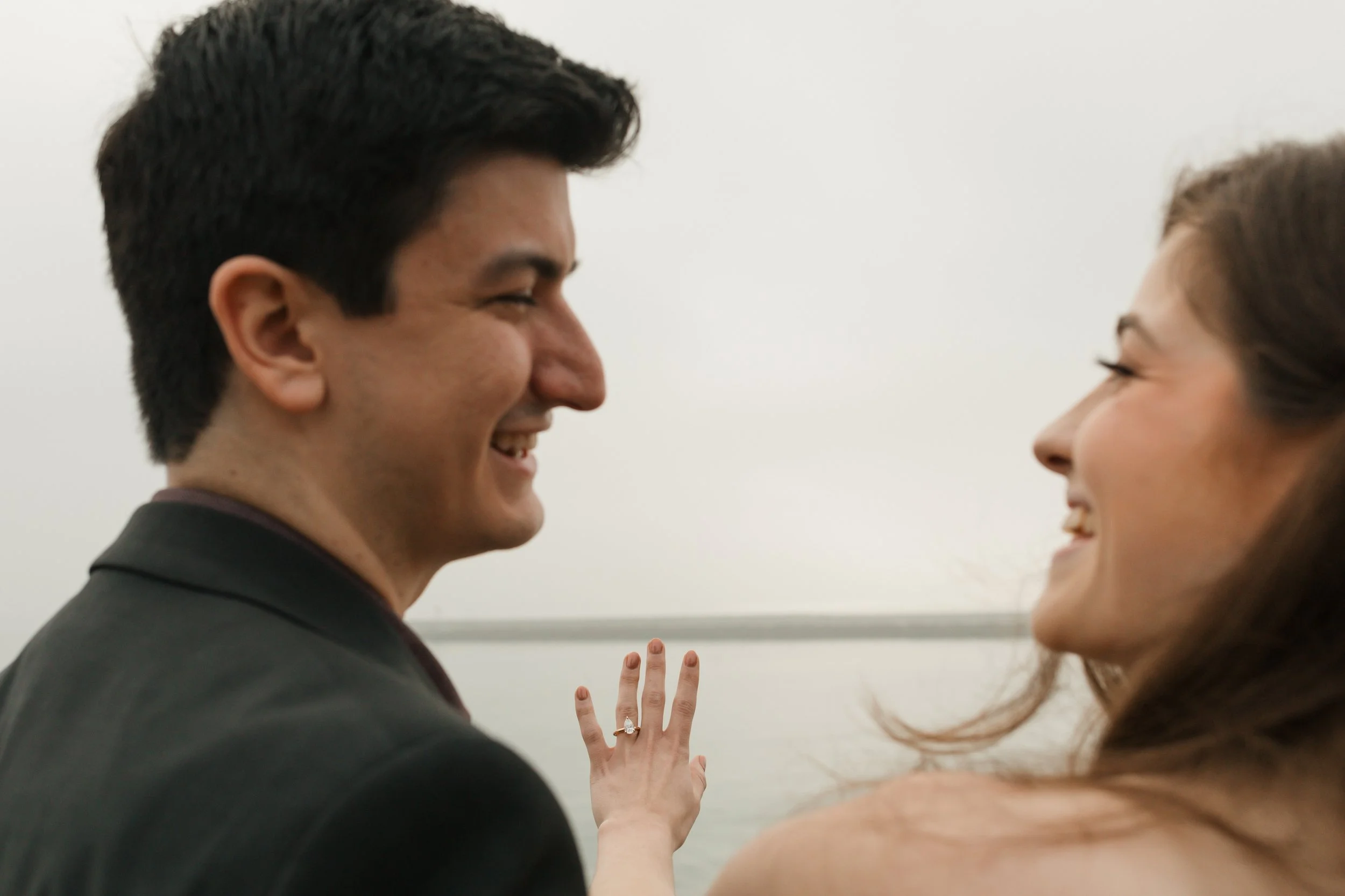 artsy photo of the couple  showing off the ring from the proposal at lookout in newport beach with the ocean in background