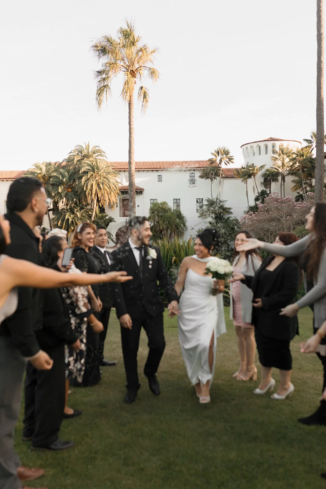 Blurry artistic candid of couple walking through a tunnel of guests made by family after ceremony at the Santa Barbara Courthouse Sunken Gardens exit celebration