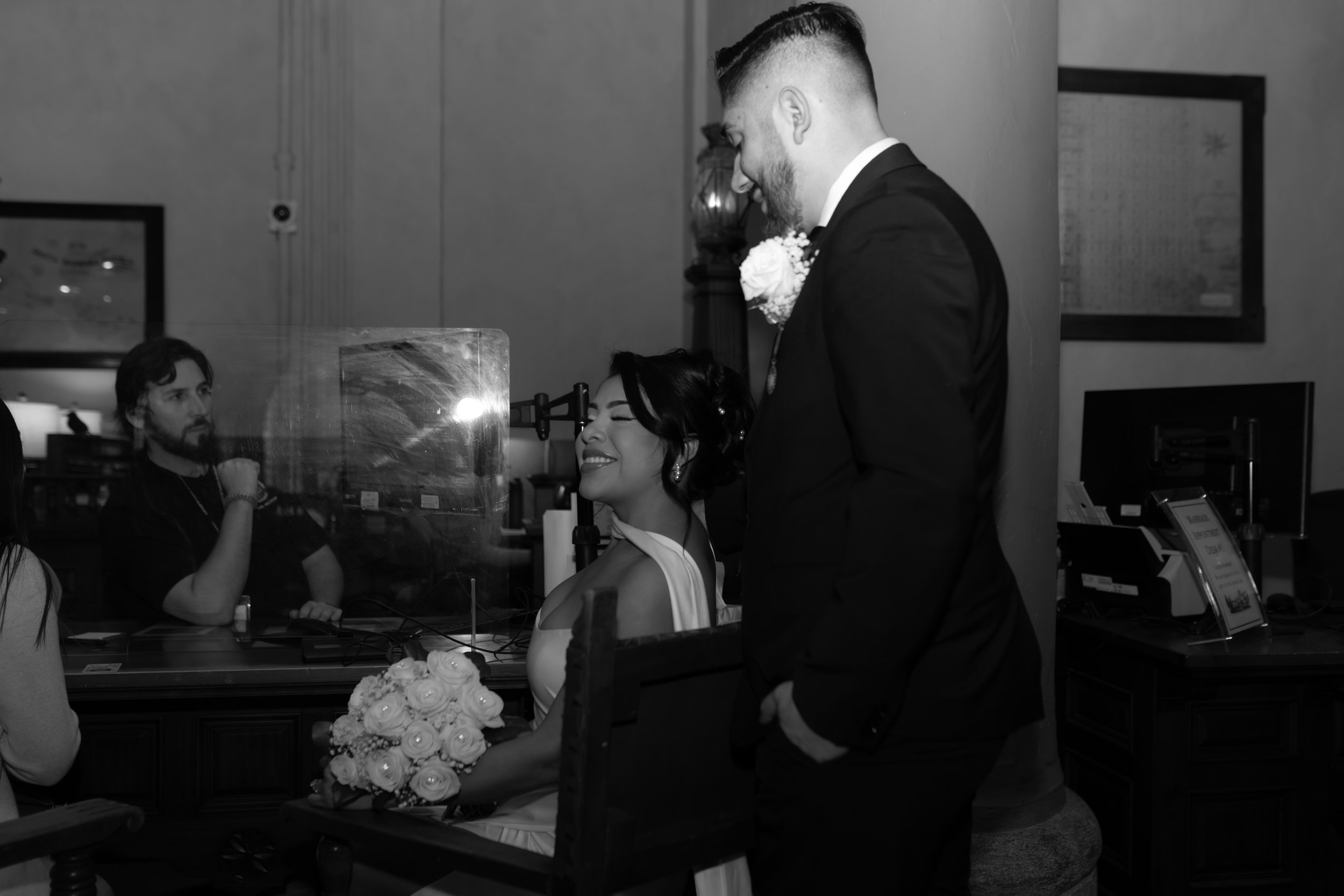 Couple embracing in a hug at the Hall of Records inside the Santa Barbara Courthouse, groom hugging bride from behind while she sits on a chair during their elopement ceremony