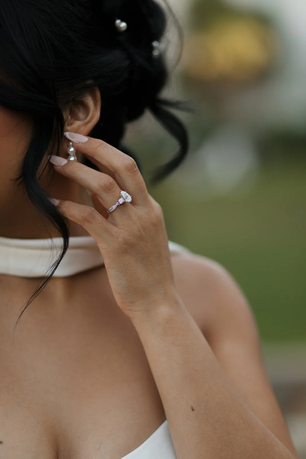 Close-up detail shot of the bride’s hand wearing her wedding ring gently holding a strand of her updo hair, highlighting delicate textures, intimate bridal styling, and soft natural light in a romantic elopement moment.