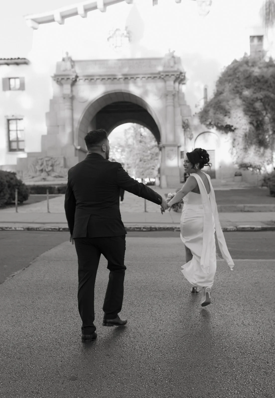 Artsy, motion-blurred photo of a couple running toward the Santa Barbara Courthouse, the bride leading and glancing back with a smile as she holds the groom’s hand behind her