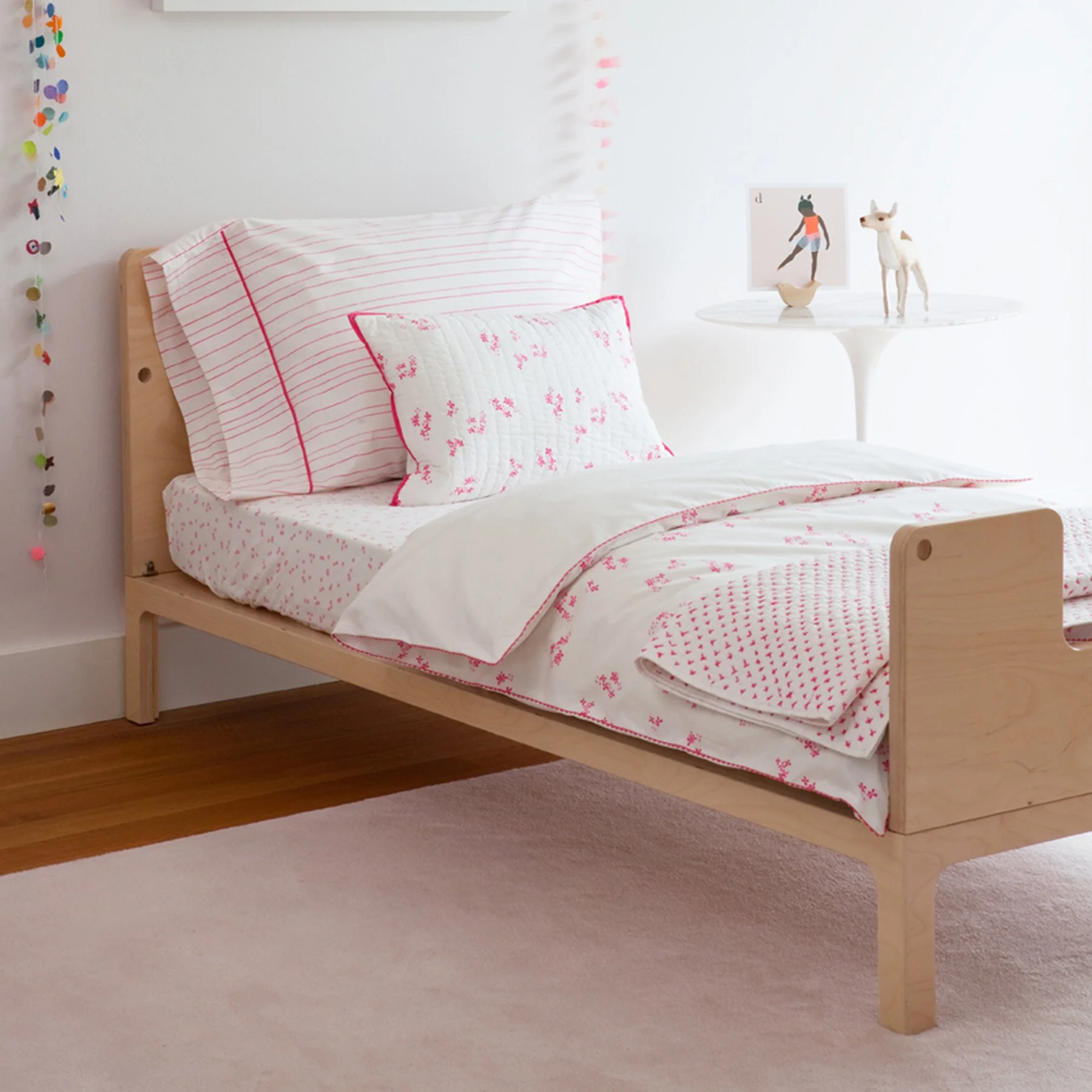 A beautiful bedroom featuring bedding with pink patterns from Little Auggie's Pretty with Pink collection designed by Gen Burgess.