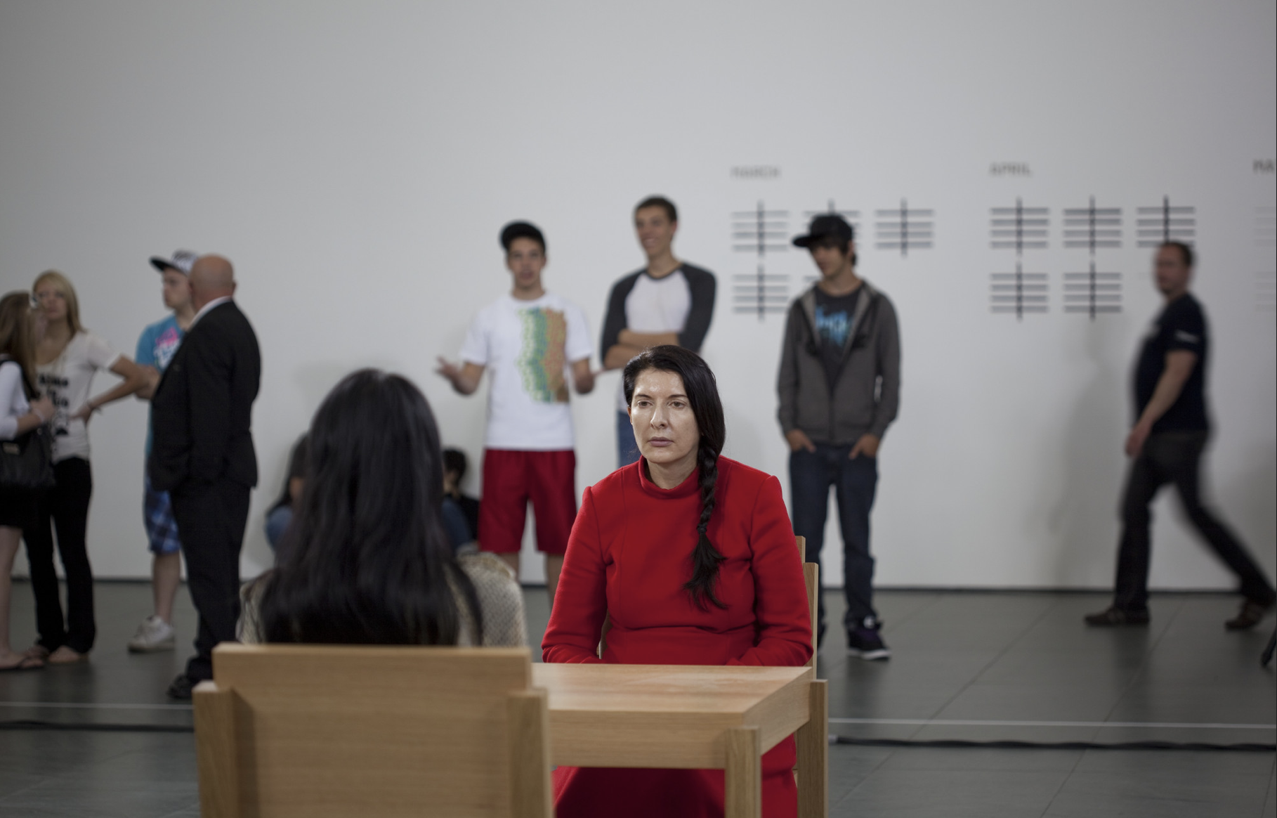 Marina Abramović in a red dress seated across a table from an audience member