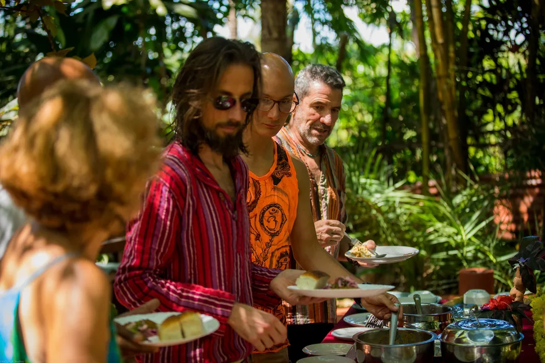 Guests serving themselves from a colorful outdoor buffet surrounded by tropical plants, highlighting wholesome, fresh retreat cuisine.