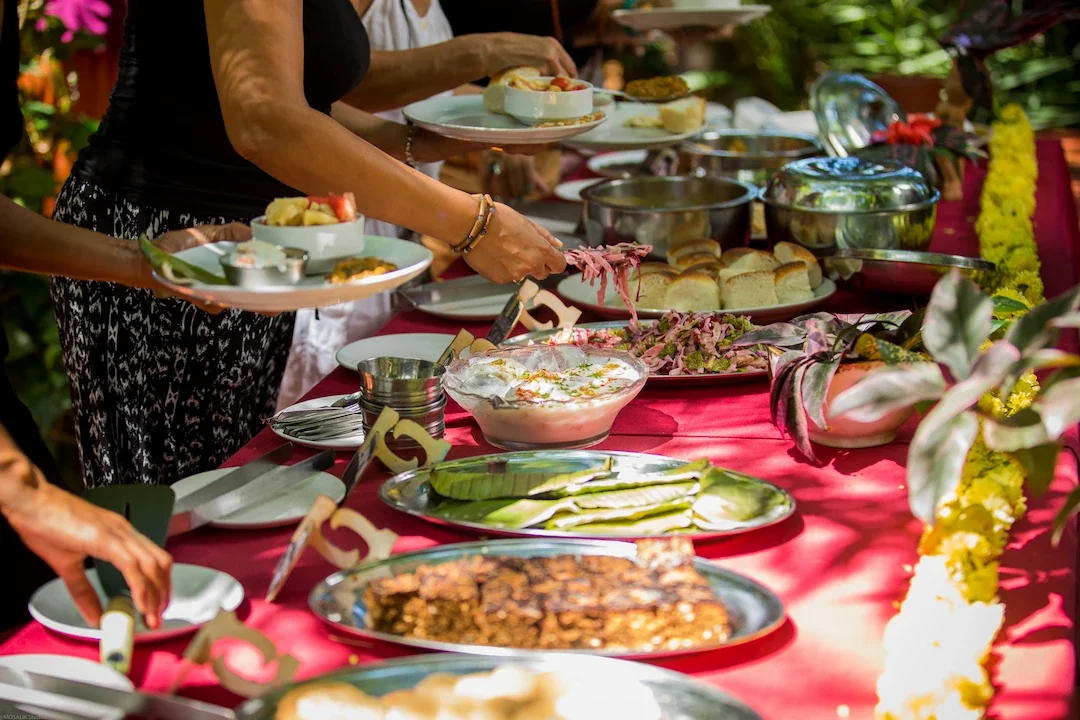 Outdoor buffet with freshly prepared dishes including salads, grilled vegetables, and yogurt-based meals, set among floral decorations and lush greenery.