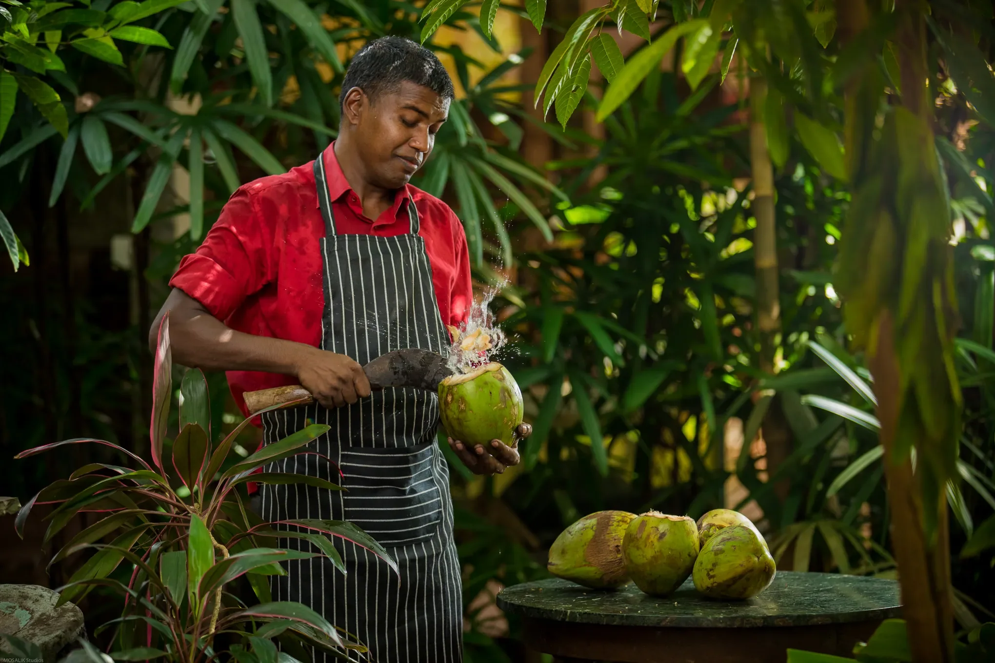 Staff member preparing fresh coconuts outdoors among tropical foliage, reflecting Bhakti Kutir’s sustainable and nature-connection