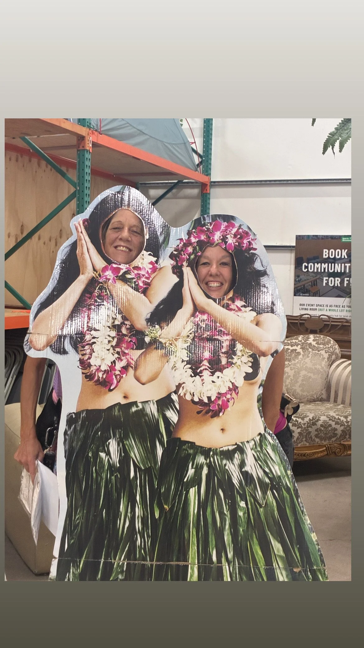  Runner Lea Genders and a friend smiling from behind cardboard cutouts of hula dancers during race packet pick up at Sports Basement for the Tiki Beach 10K. 