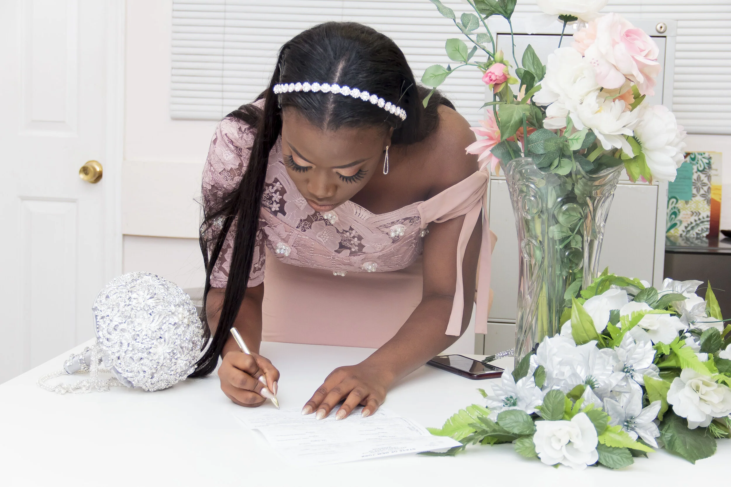 Woman signing a document at a table decorated with white flowers and a large vase of pink and white flowers.