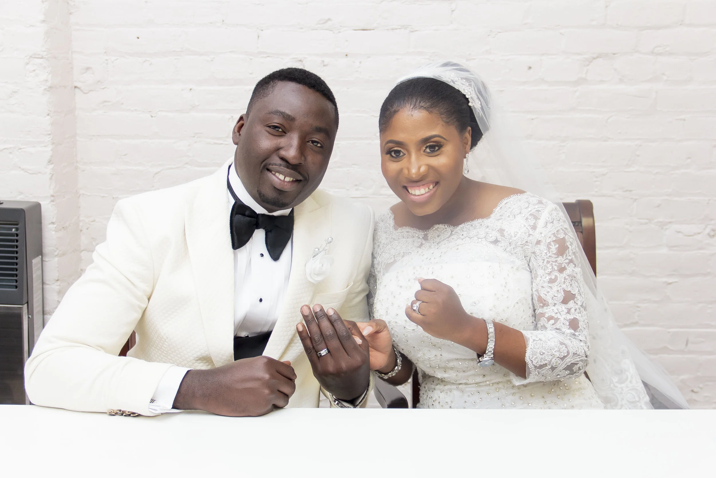 A newlywed couple dressed in wedding attire showing their wedding rings and holding hands.