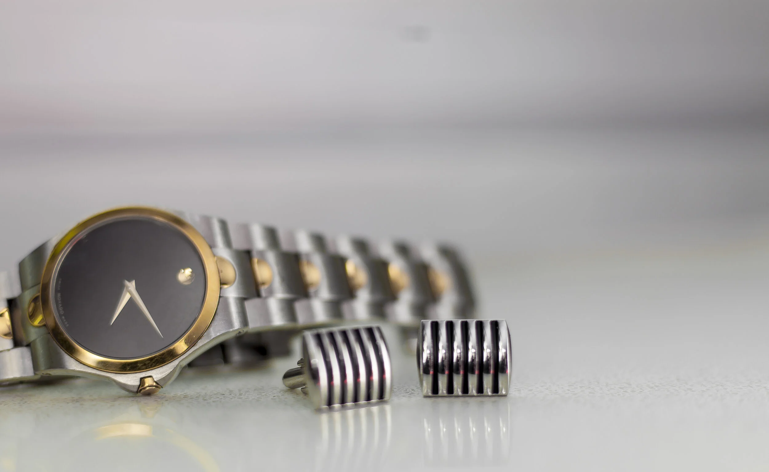 Close-up of a wristwatch with a metallic band and a dark face, and two metallic vent-like objects on a speckled surface.