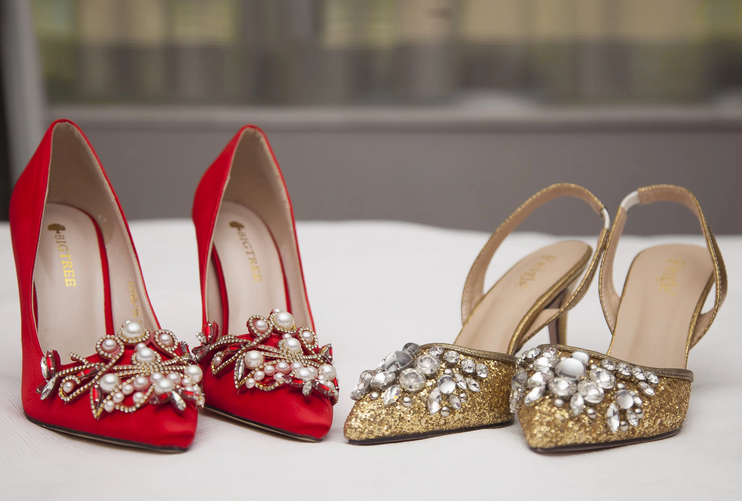 A collection of high heel shoes, including red and gold pairs, decorated with pearls and rhinestones, displayed on a white surface.