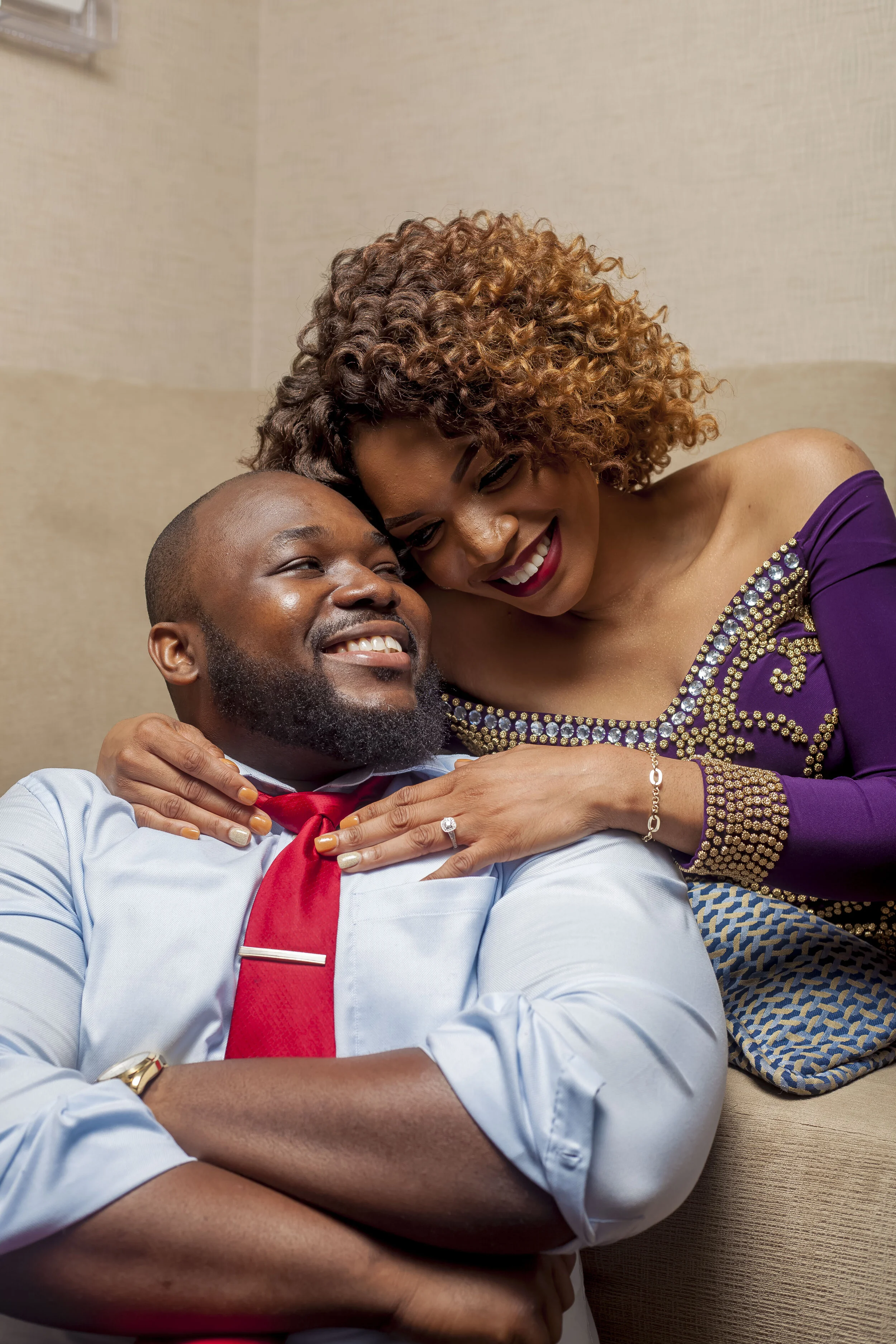 A couple smiling happily, with the woman leaning her head on the man's shoulder, in a warm indoor setting.