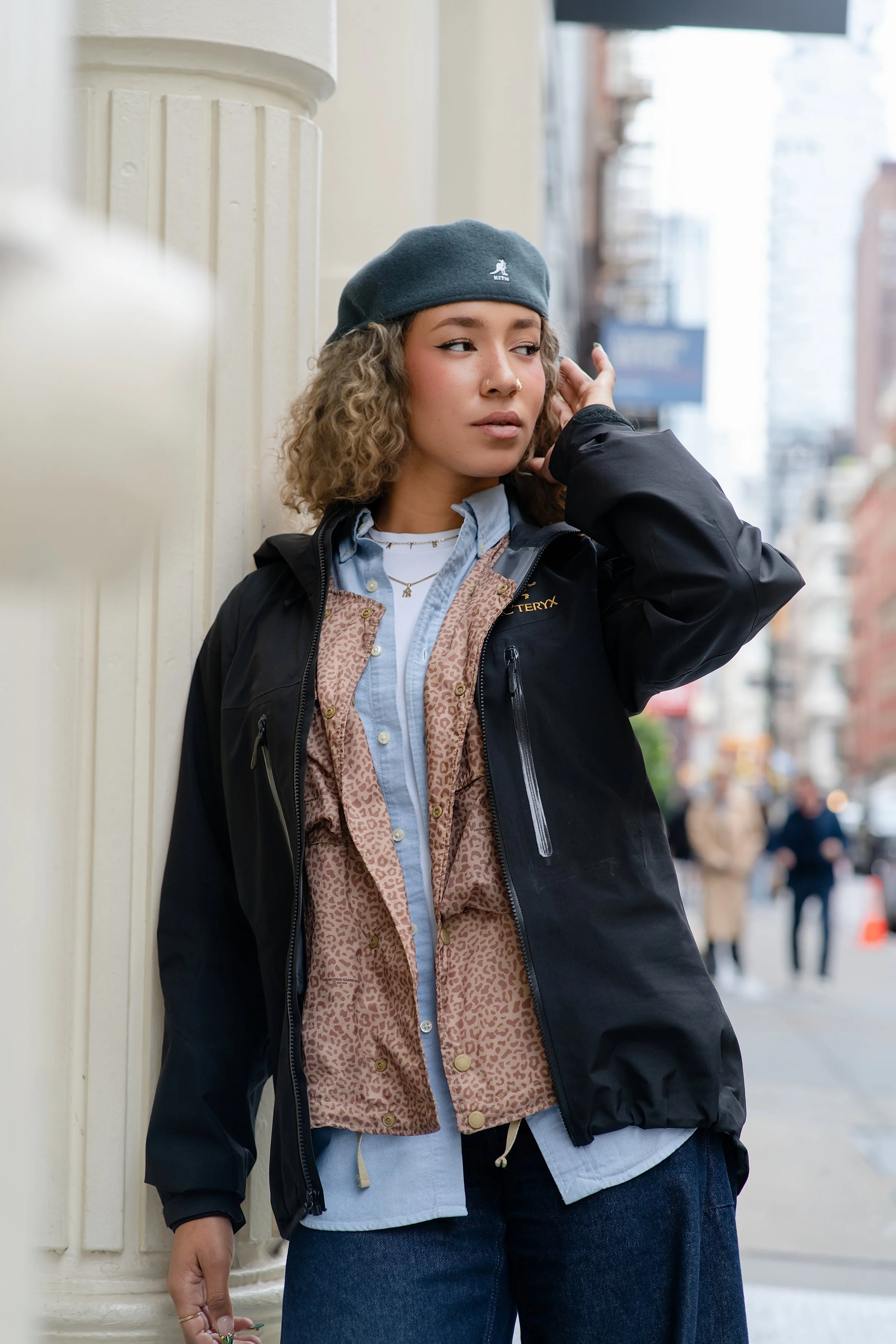 Fashion portrait of a woman in a cap and dark jacket standing on a city street