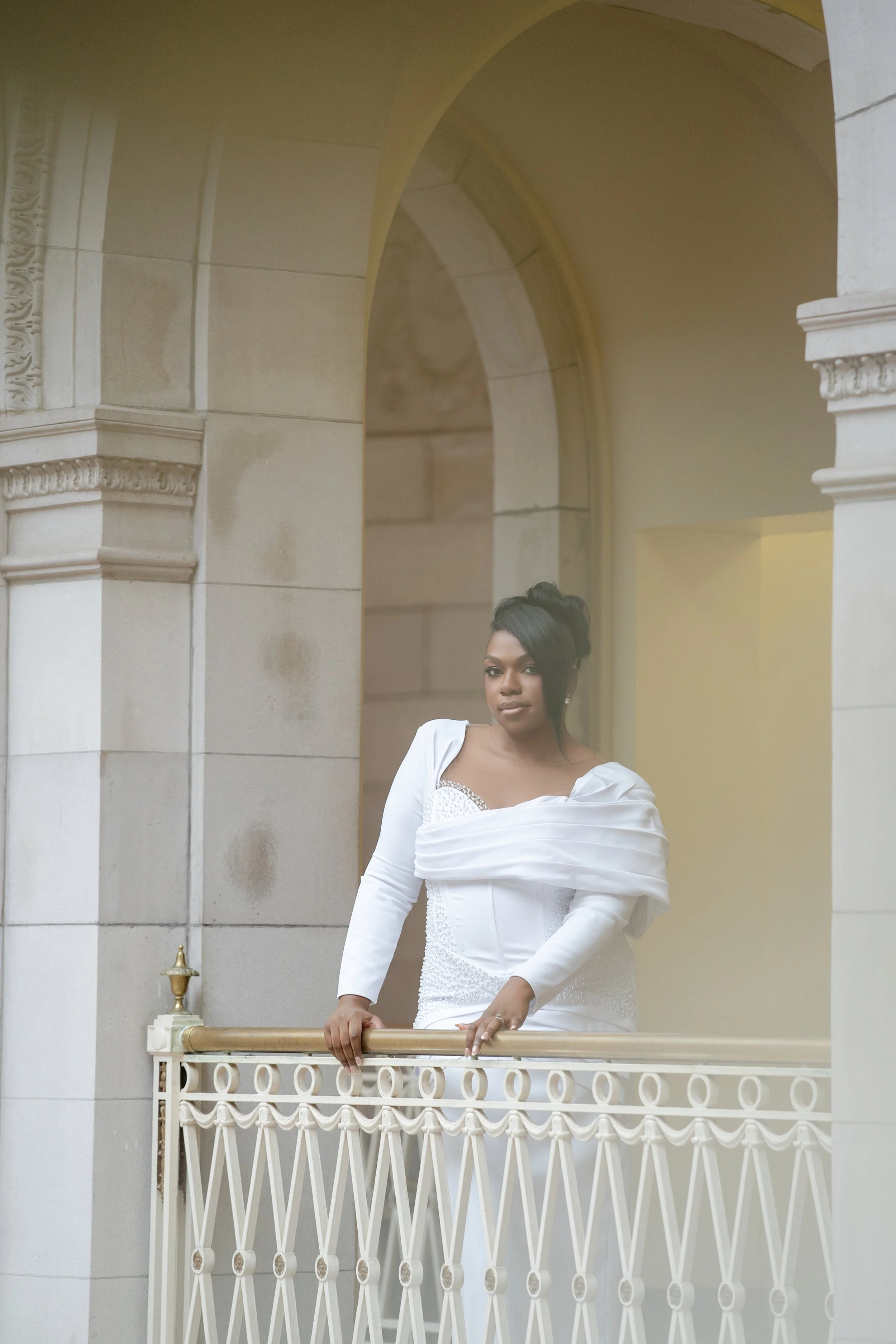 Bride in a white dress posing beside an ornate balcony during a wedding portrait