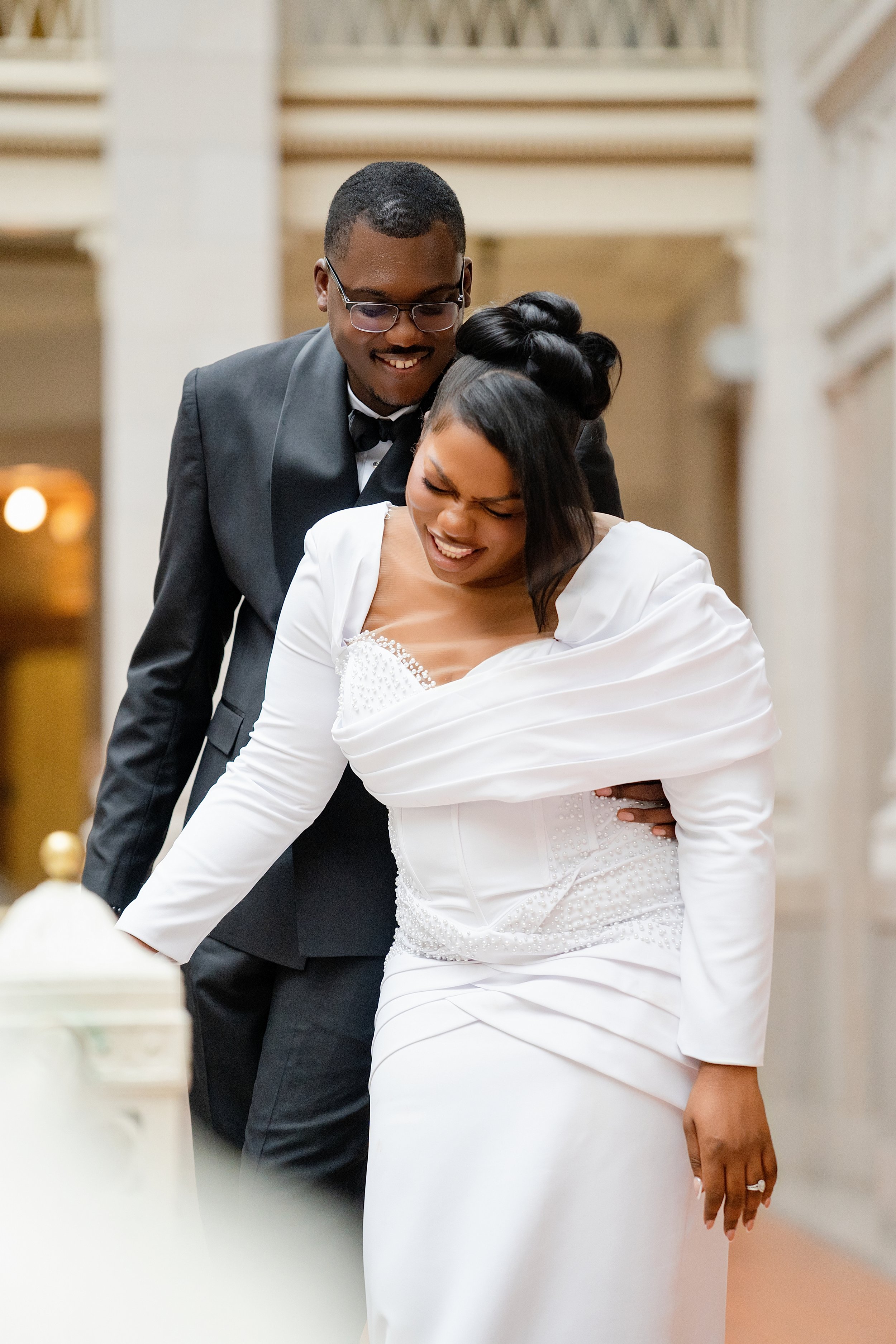 Bride seated in a white wedding dress with the groom standing behind her during a wedding portrait