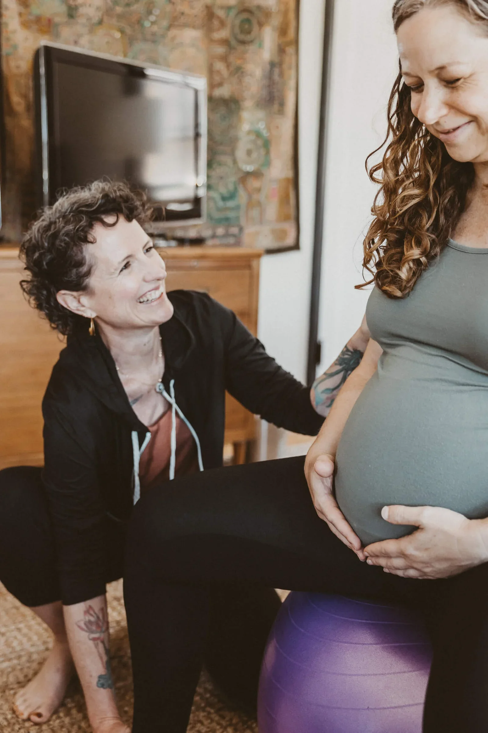 A doula gently touches a pregnant person while they laugh together.