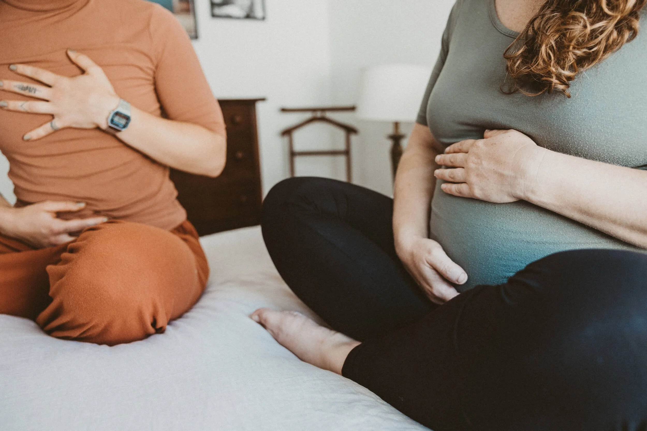 Childbirth education class teacher in orange on left demonstrating a breathing technique to a pregnant person in green on the right who is holding her belly similarly.
