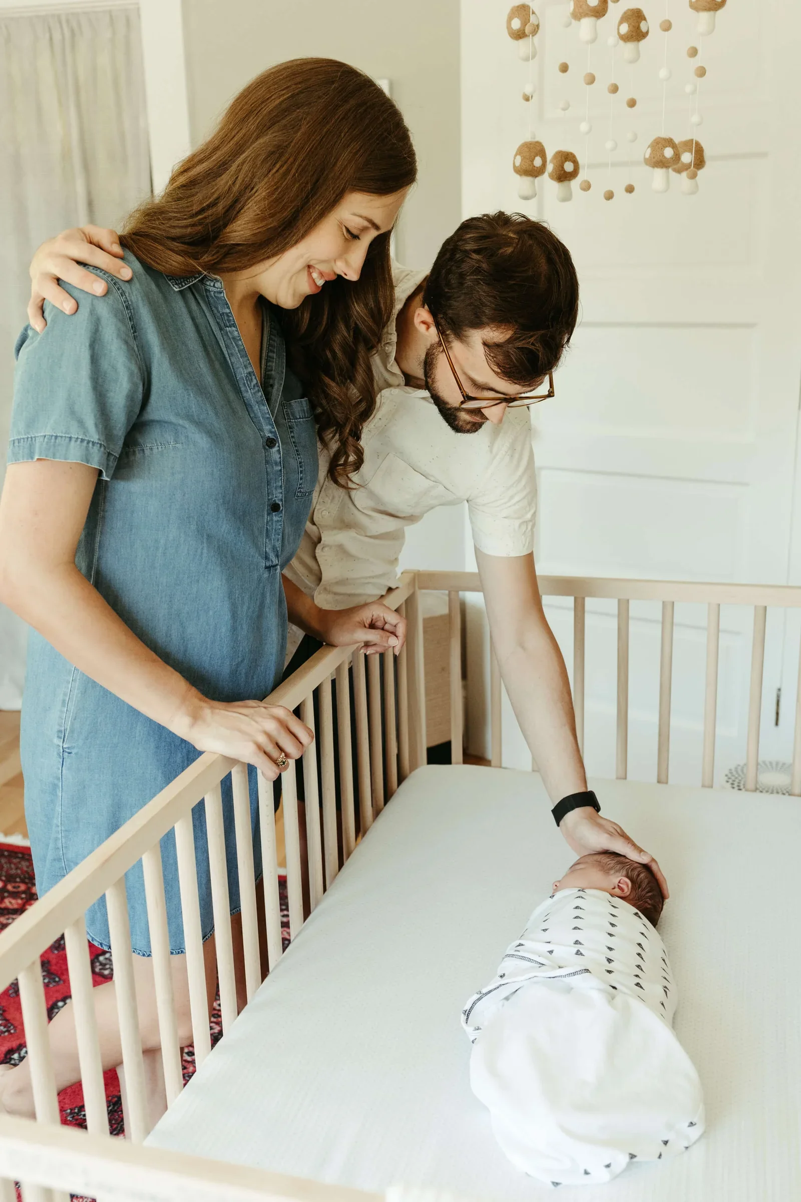 A Portland postpartum doula supports new parents as they admire their swaddled newborn in a peaceful nursery, capturing a tender moment of connection and care during the early days of parenthood.