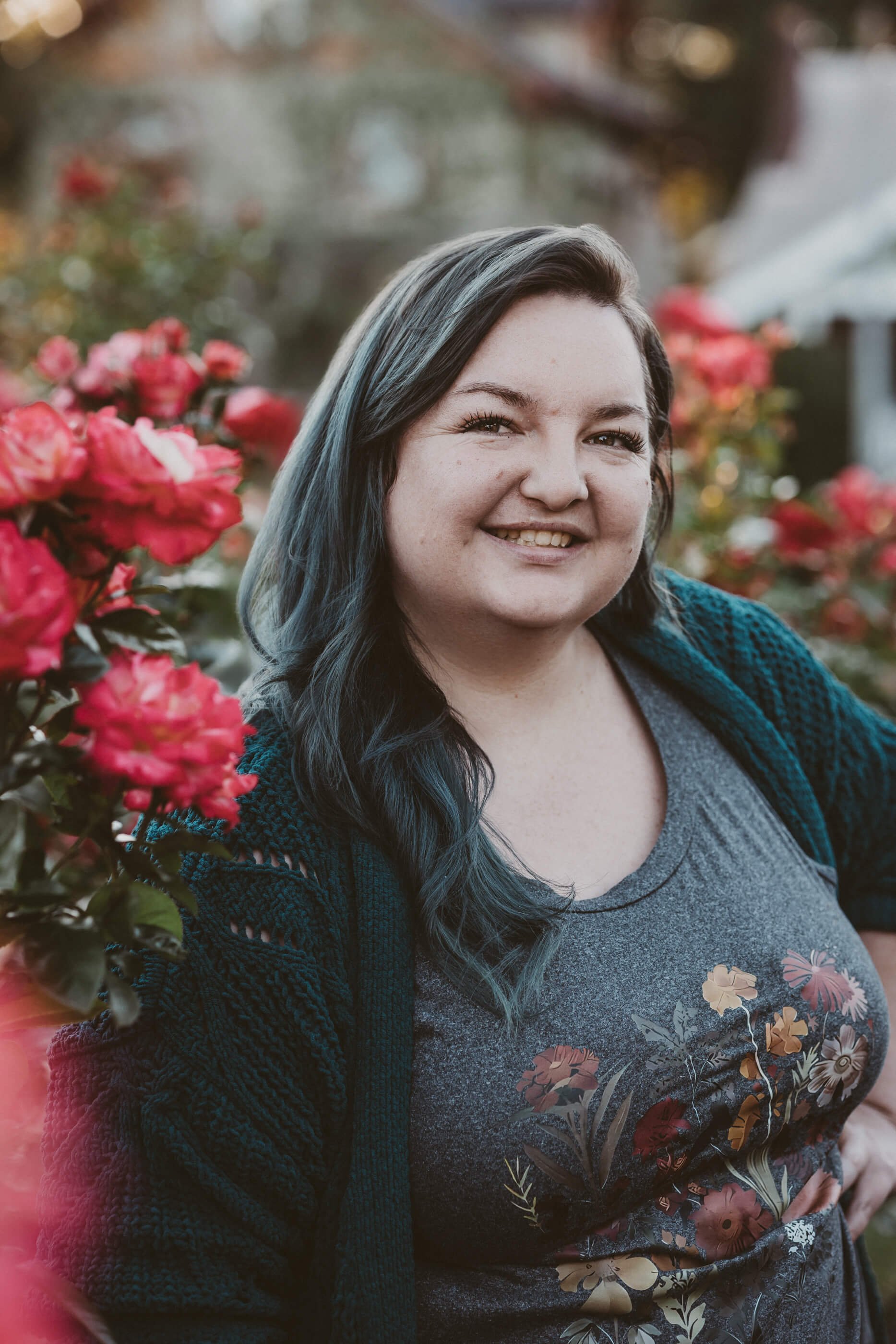 Portland postpartum doula Kimmi Burke stands smiling warmly at the camera, surrounded by blooming Portland roses.