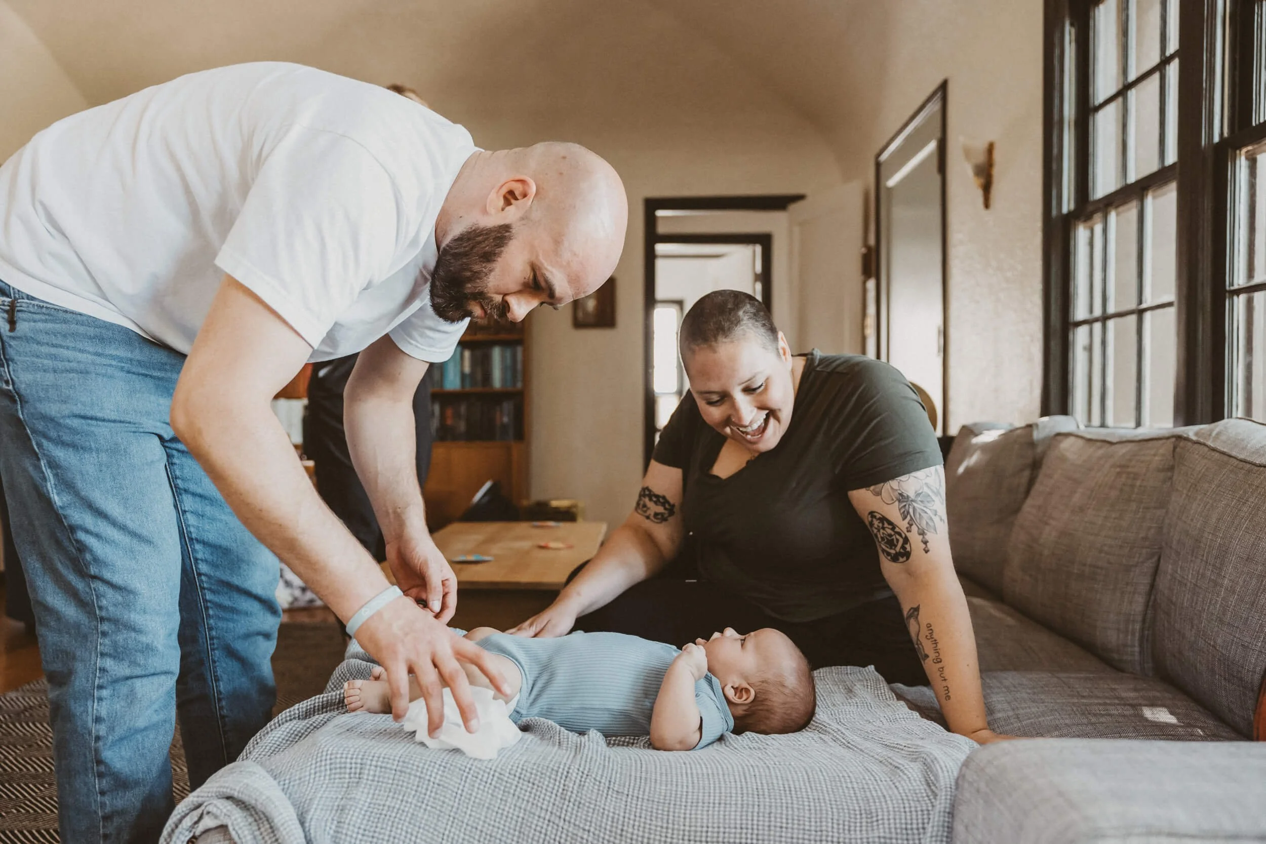 Newborn care educator looks on happily as a dad finishes changing his baby's diaper in baby class.