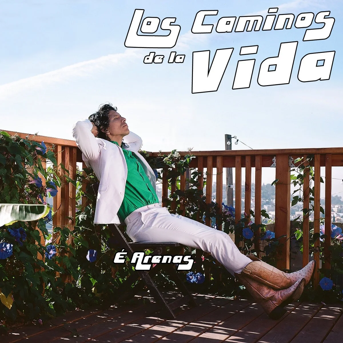 A man dressed in a white suit and green shirt sitting on a balcony surrounded by flowers, looking up towards the sky with a relaxed expression, under a blue sky with a few clouds. The text on the image reads "Los Caminos de la Vida" and "É Incas".