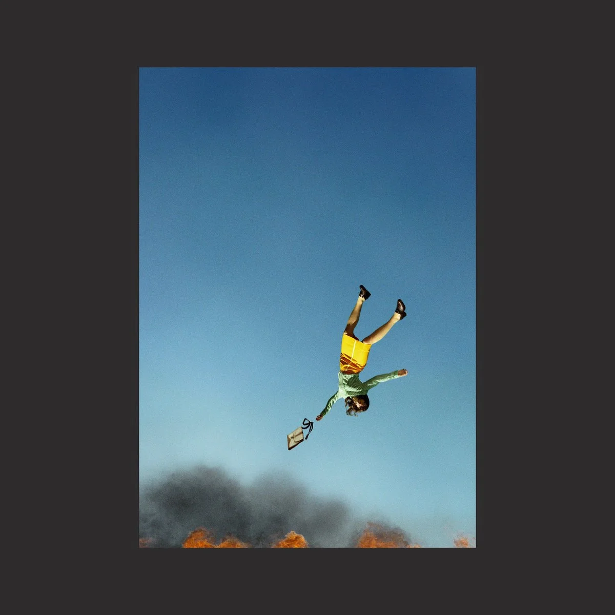 A person falling from the sky, holding a briefcase, with fire and smoke below and a clear blue sky above.