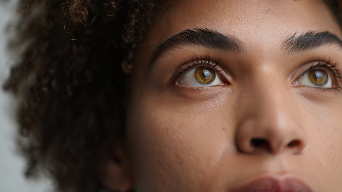  An extremely close-up, highly detailed portrait focusing on the eyes and face of a woman with curly dark hair. The shot is framed from the side, looking up towards the eyes. The subject's light brown or amber-colored eyes are the main focus, with a 