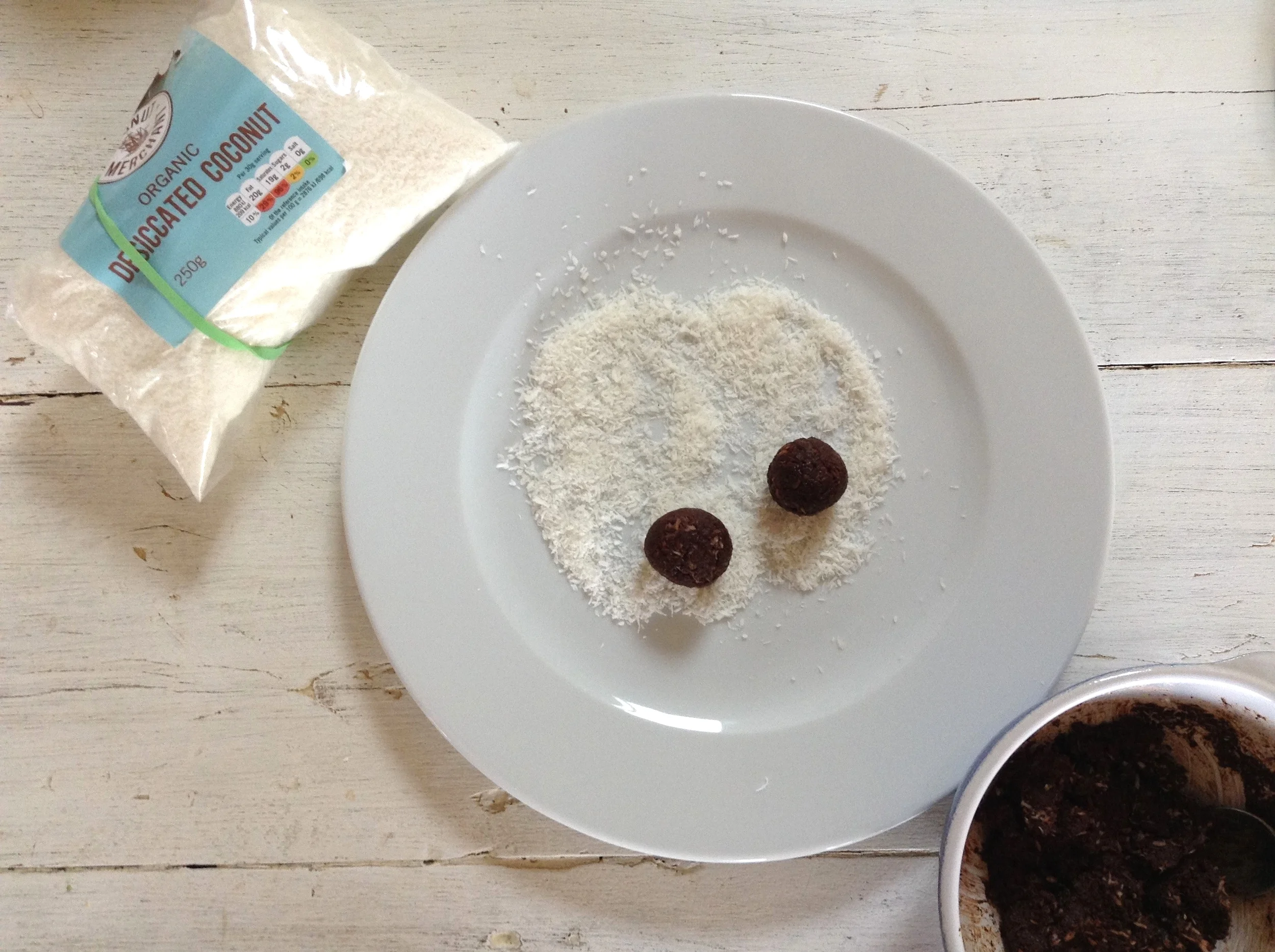 The mixture has been chilled and formed into balls. Coconut Shreds have been placed on a plate, and the truffles are ready to roll! Literally.