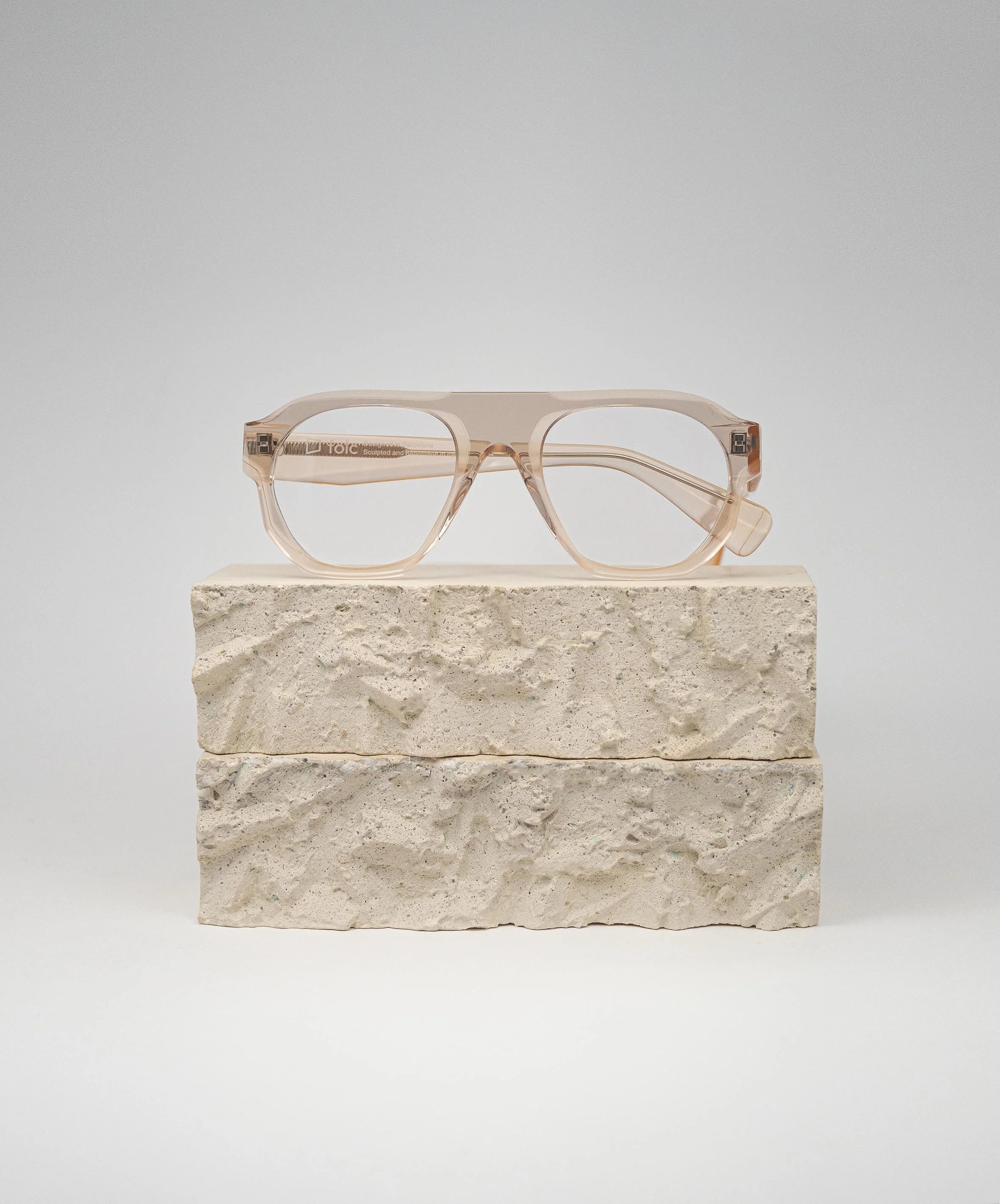 A pair of pink translucent eyeglasses rests on top of three stacked rough-textured white stone blocks against a plain light gray background.