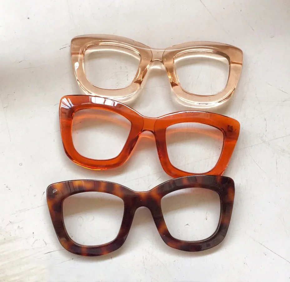 Three pairs of vintage-style eyeglasses with square frames in light, orange, and dark tortoise patterns laid out on a white surface.