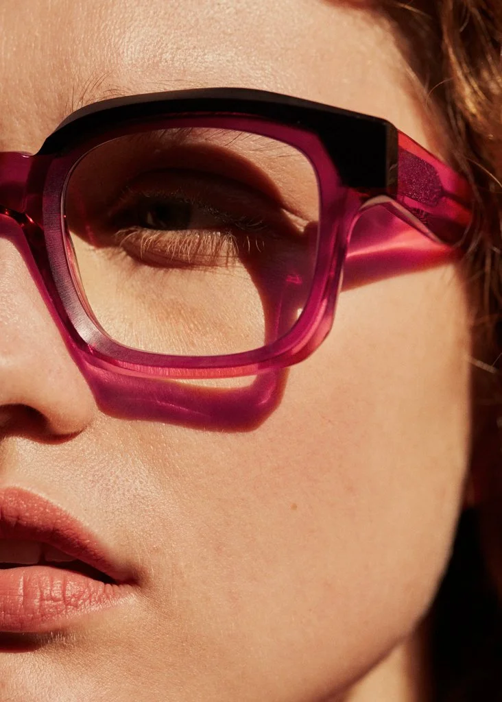 Close-up of a person's face wearing pink sunglasses, showing part of the eye, nose, and lips.