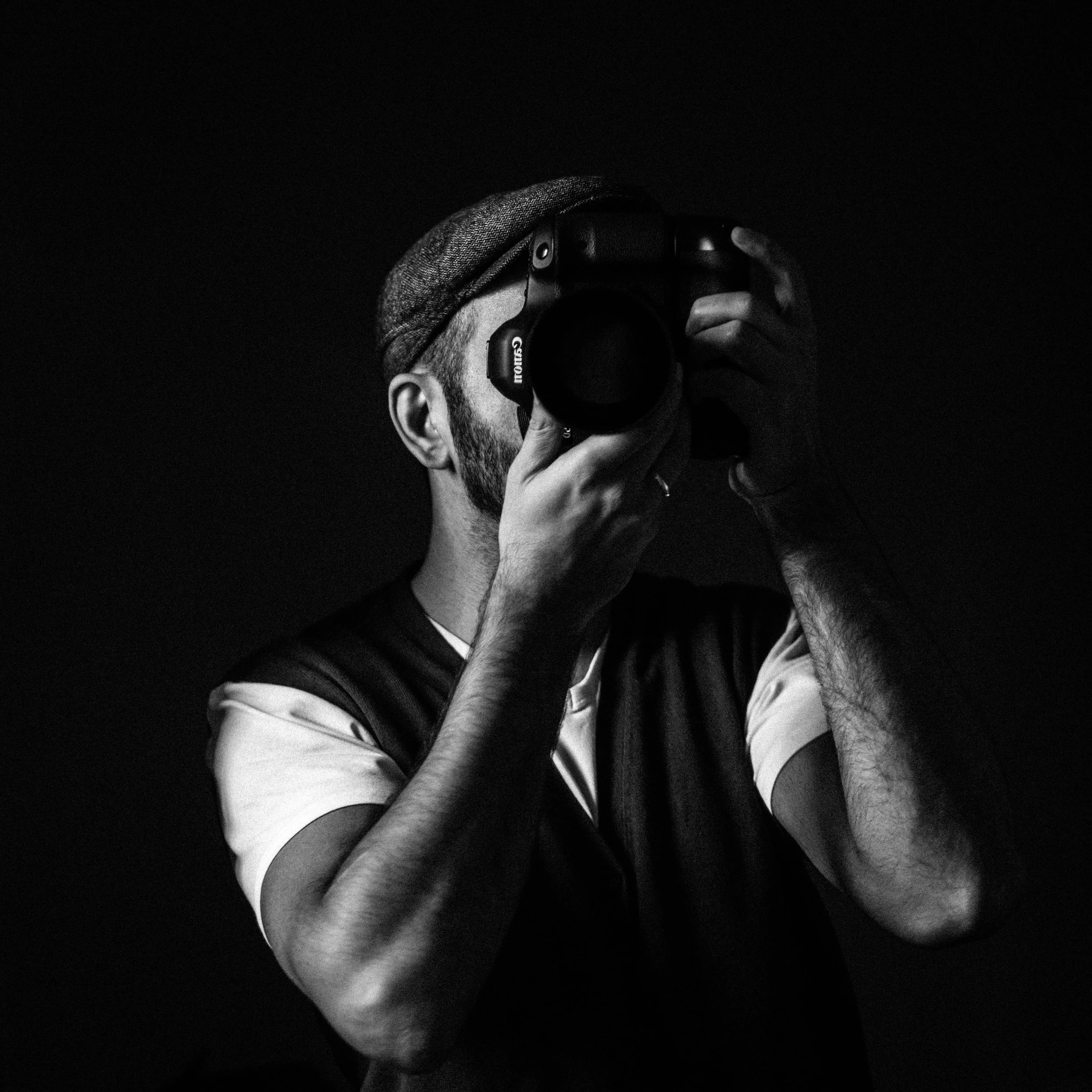 A person wearing a hat and headphones, holding a camera, taking a photo in a dark setting.