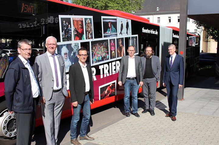 "Ab sofort rollen die Künstler des Trierer Theater-Ensembles Tag und Nacht durch die Straßen der Stadt. Zwei Linienbusse der Stadtwerke Trier (SWT) wurden mit großflächigen Prints beklebt und zeigen bunte Spielszenen und Akteure der Trierer Theaterwelt. Zu diesem besonderen Anlass fand heute bei strahlendem Sonnenschein ein Pressetermin vor dem Theater statt. Foto v.li. Busfahrer Jens Korn, Oberbürgermeister Wolfram Leibe, Beigeordneter Thomas Schmitt, Verwaltungsdirektor Herbert Müller, Chefdisponent Marius Klein-Klute und SWT-Vorstand Dr. Olaf Hornfeck".