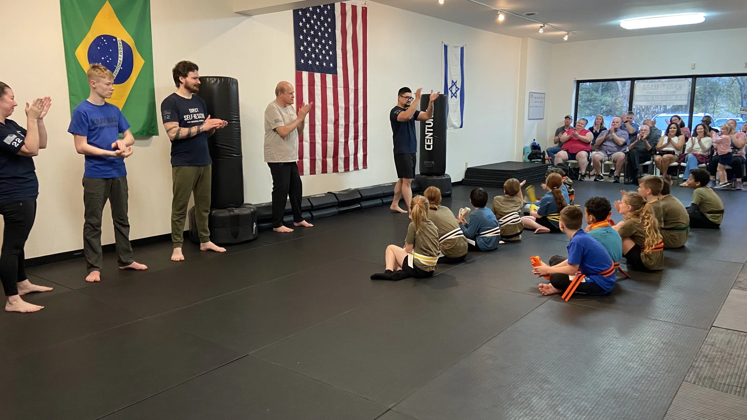 Young girl practicing martial arts with an instructor in a martial arts class, with other children in the background.