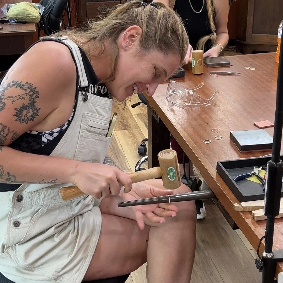 Student hammering a handmade sterling silver stacking ring at the jeweler's bench.